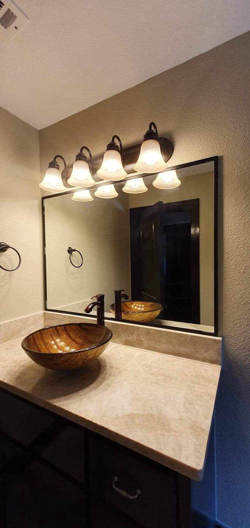 Bathroom vanity with vessel sink, mirror, and light fixture. The countertop is beige, and the sink is brown.