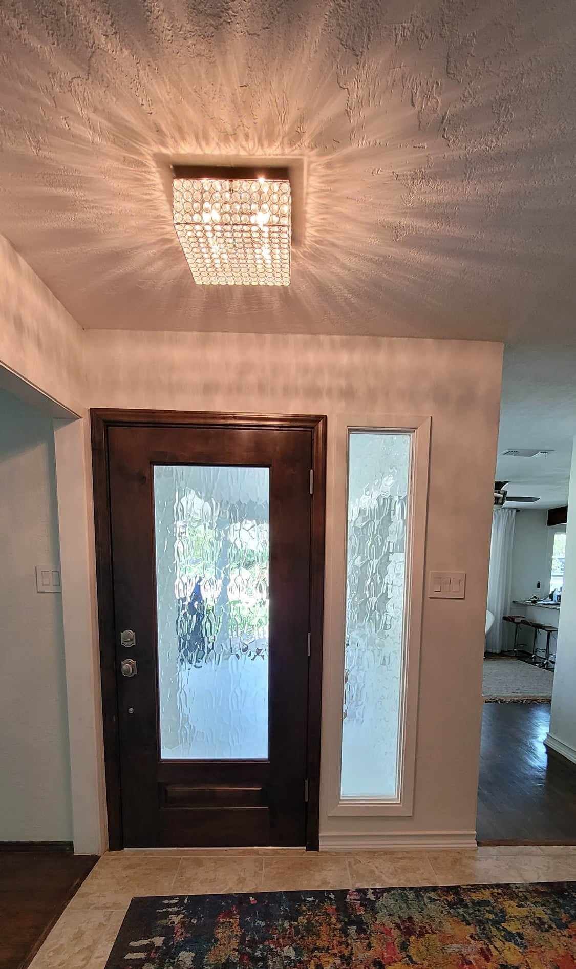 Entryway with dark wooden door and frosted sidelight, under a square crystal chandelier.