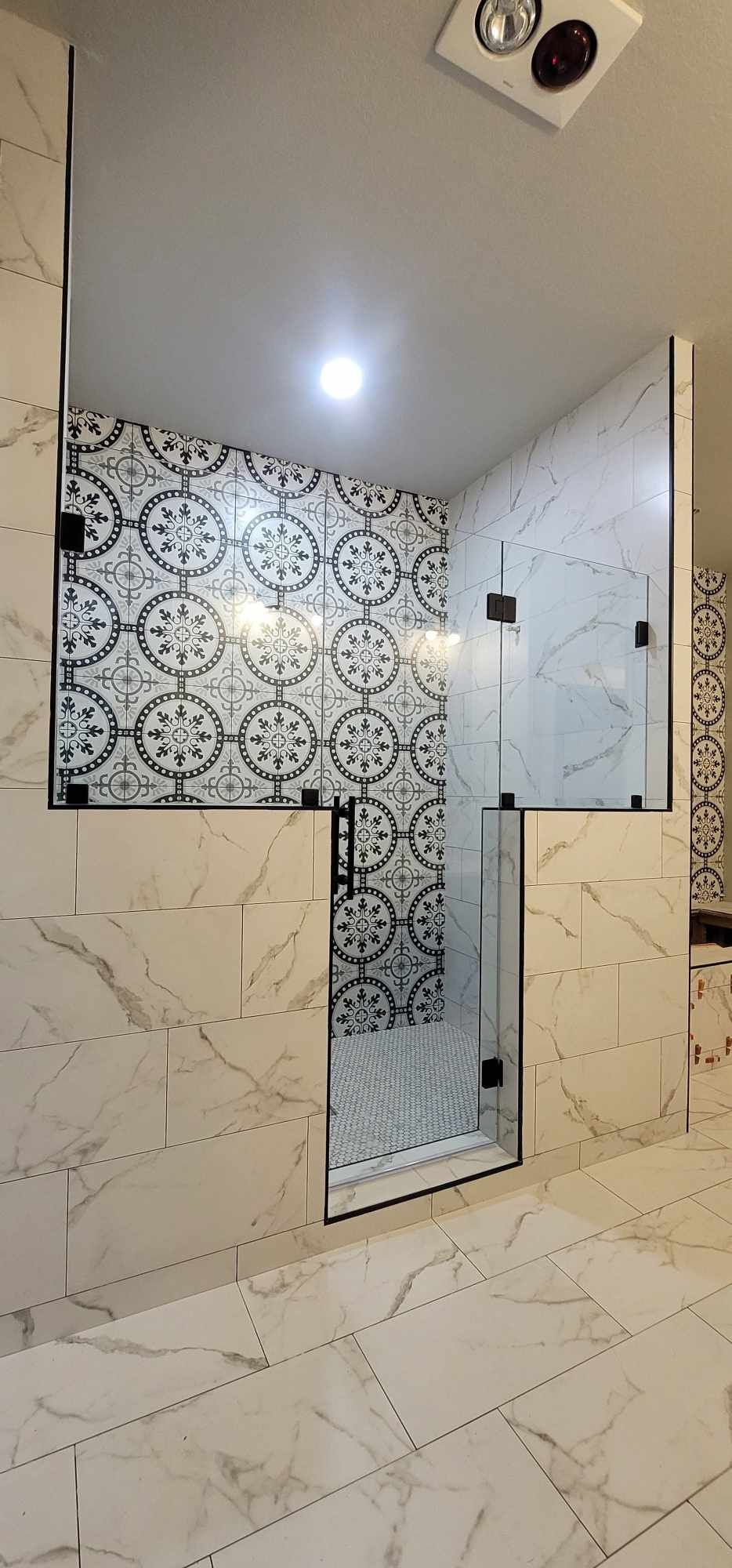 A modern shower with white marble walls and flooring, glass doors, and a decorative tile accent wall.