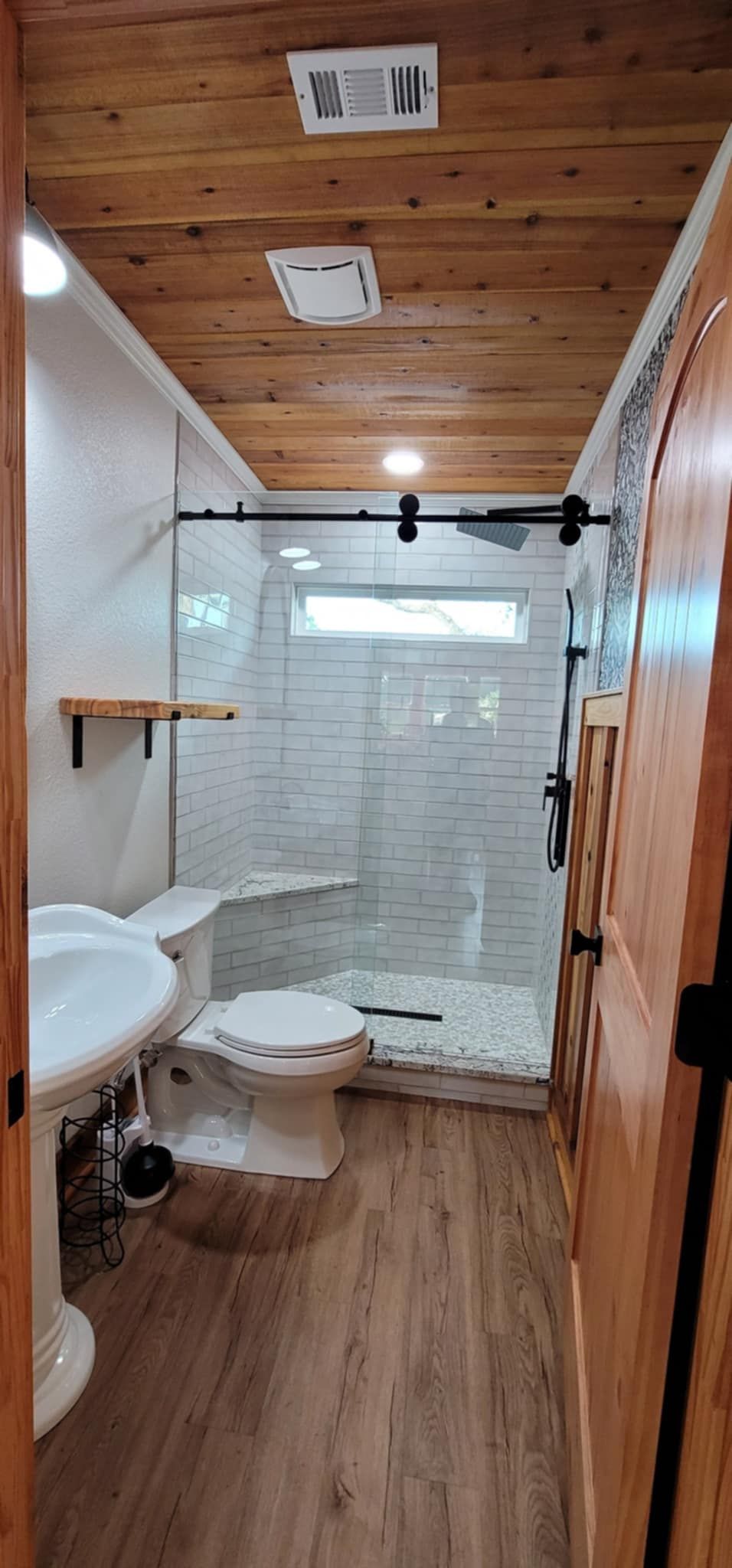 Narrow bathroom with wood ceiling and floor, white tiled shower, toilet, and sink.