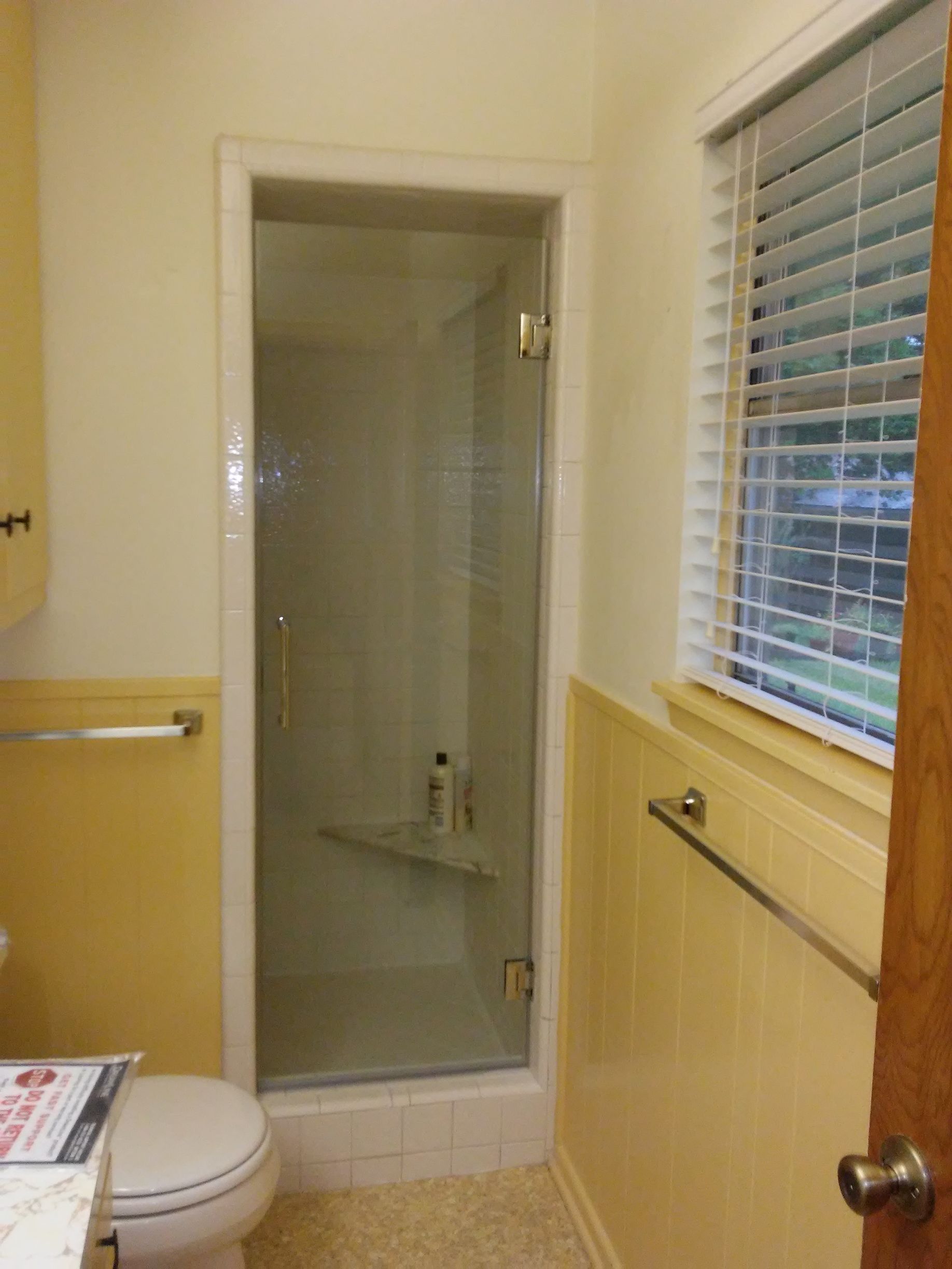 Bathroom with a glass shower, yellow tile walls, toilet, and a window with blinds.