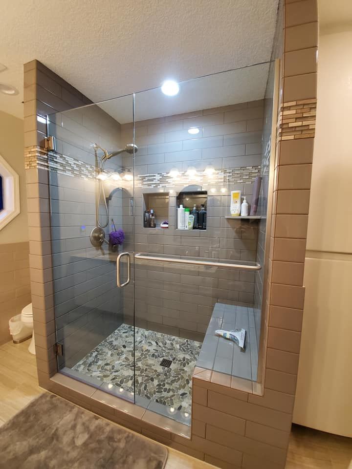Modern shower with glass door, stone floor, built-in bench, tiled walls, and recessed shelves.
