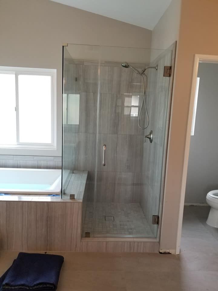 Bathroom with glass shower enclosure, gray tiled walls, bathtub, and toilet visible.