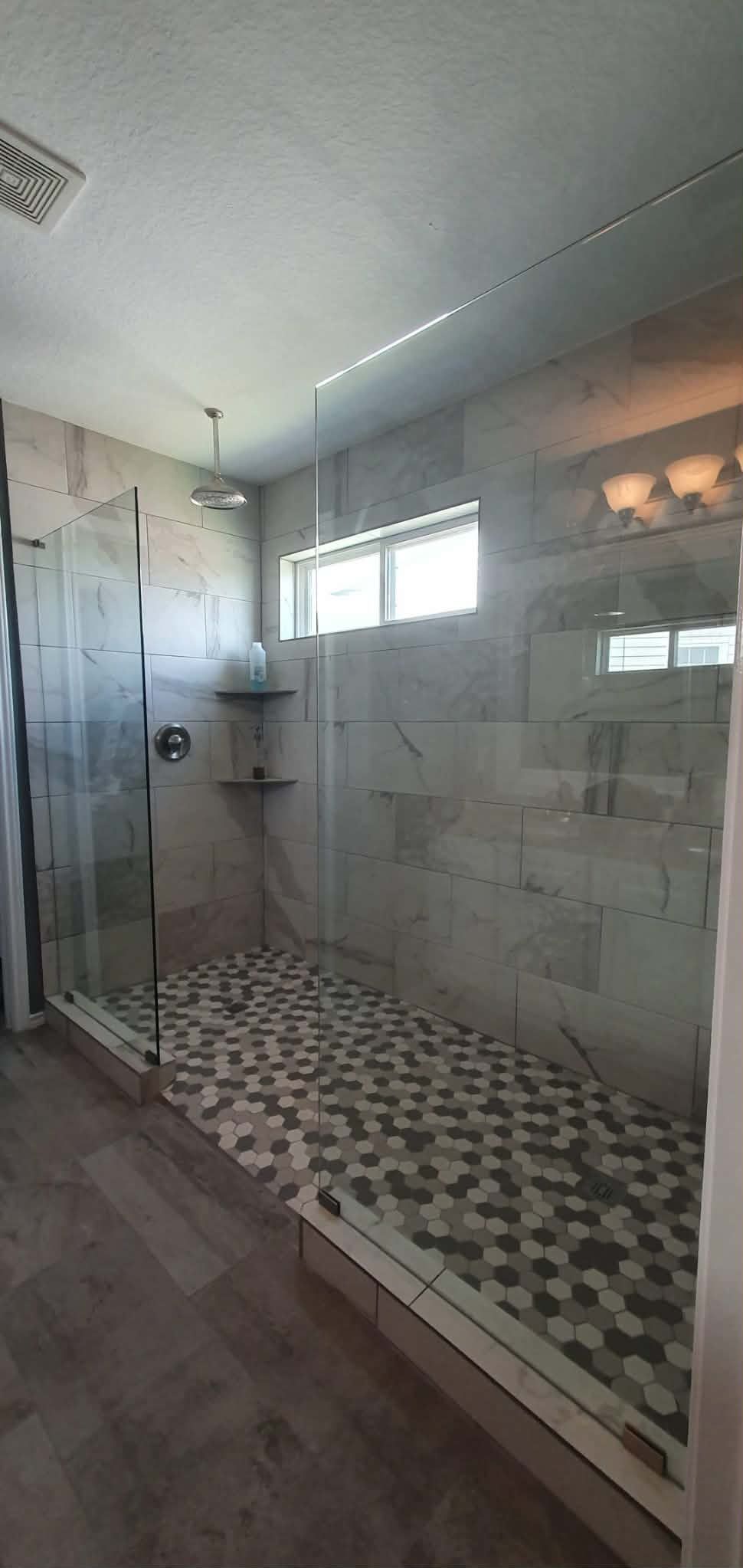 Spacious modern shower with glass door. Gray stone tile and pebble shower floor.