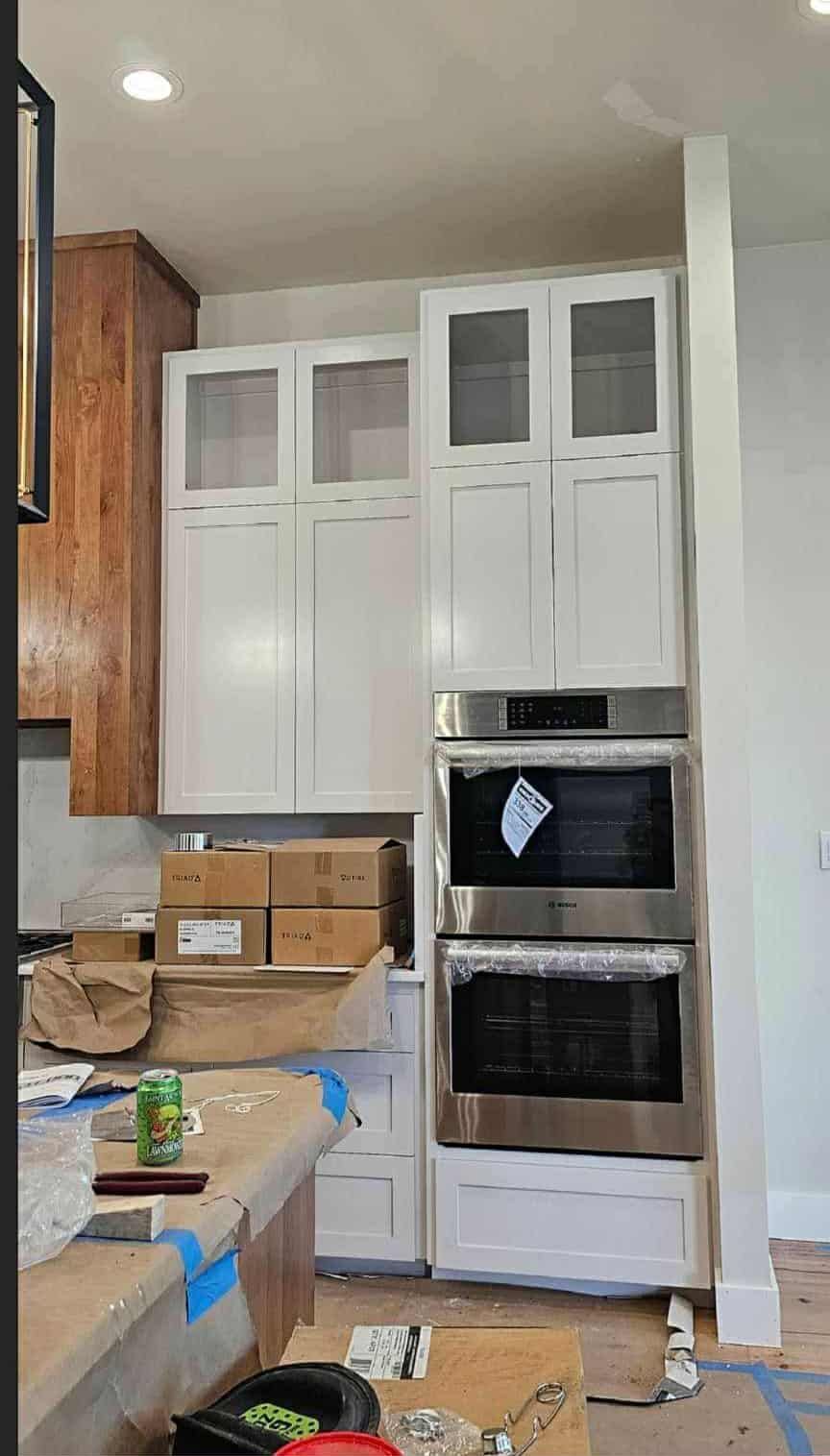 White kitchen cabinets with built-in stainless steel oven. Construction in progress.