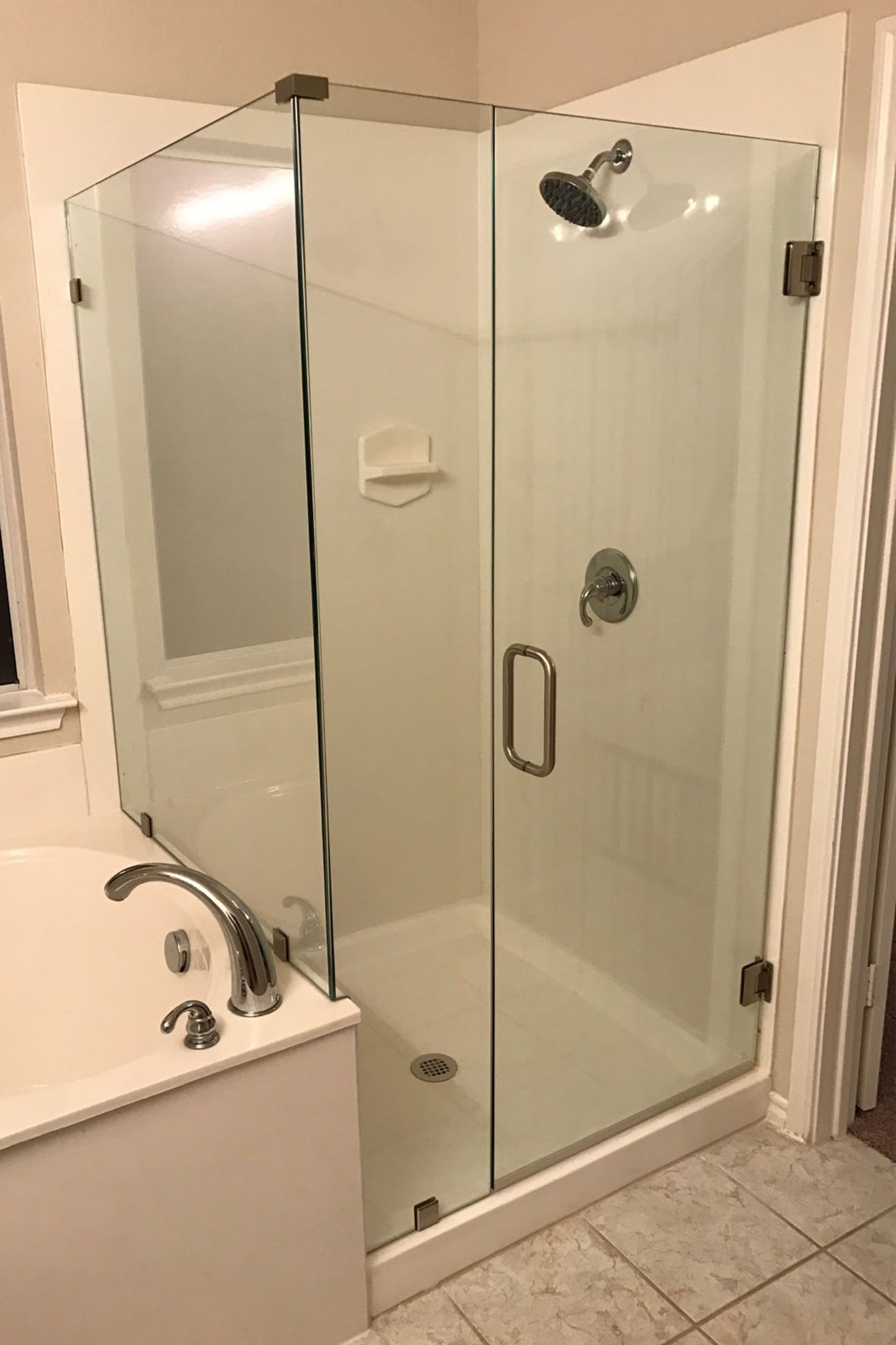 Glass shower enclosure in a bathroom, with white walls and a tub nearby.