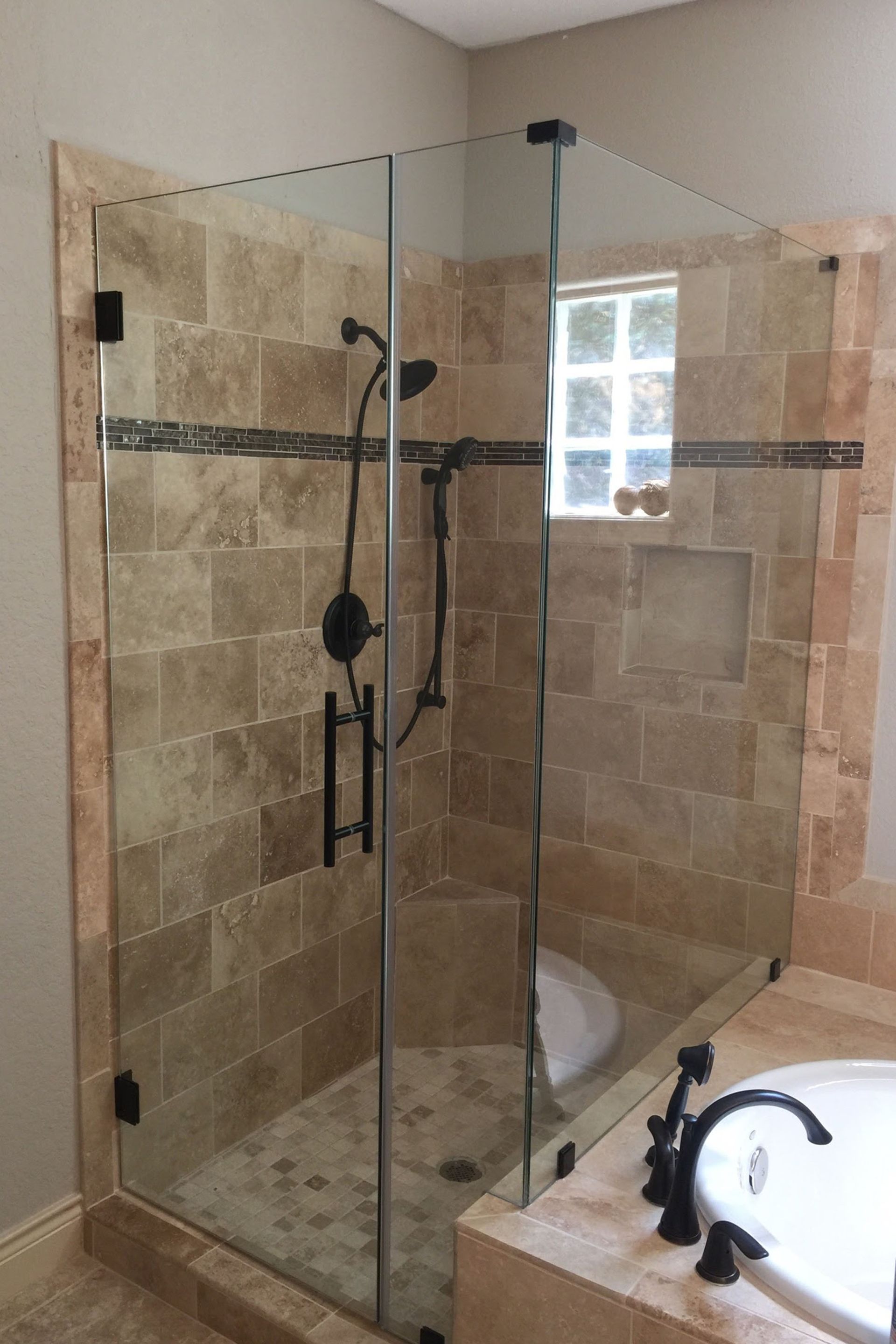 Glass shower enclosure with black hardware, beige tile walls, and a recessed window.