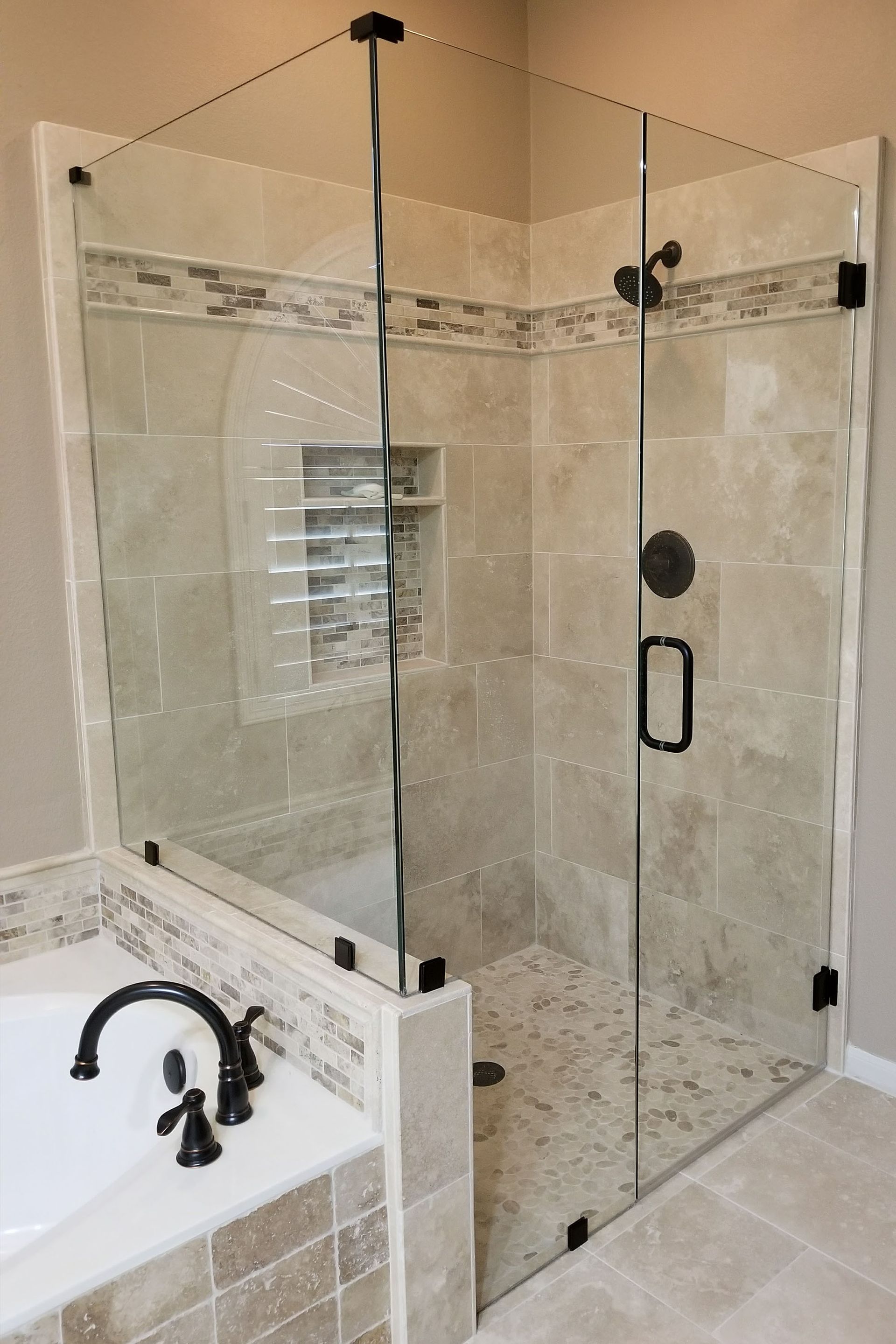 Glass shower enclosure with black hardware, beige tiled walls, and pebble flooring.