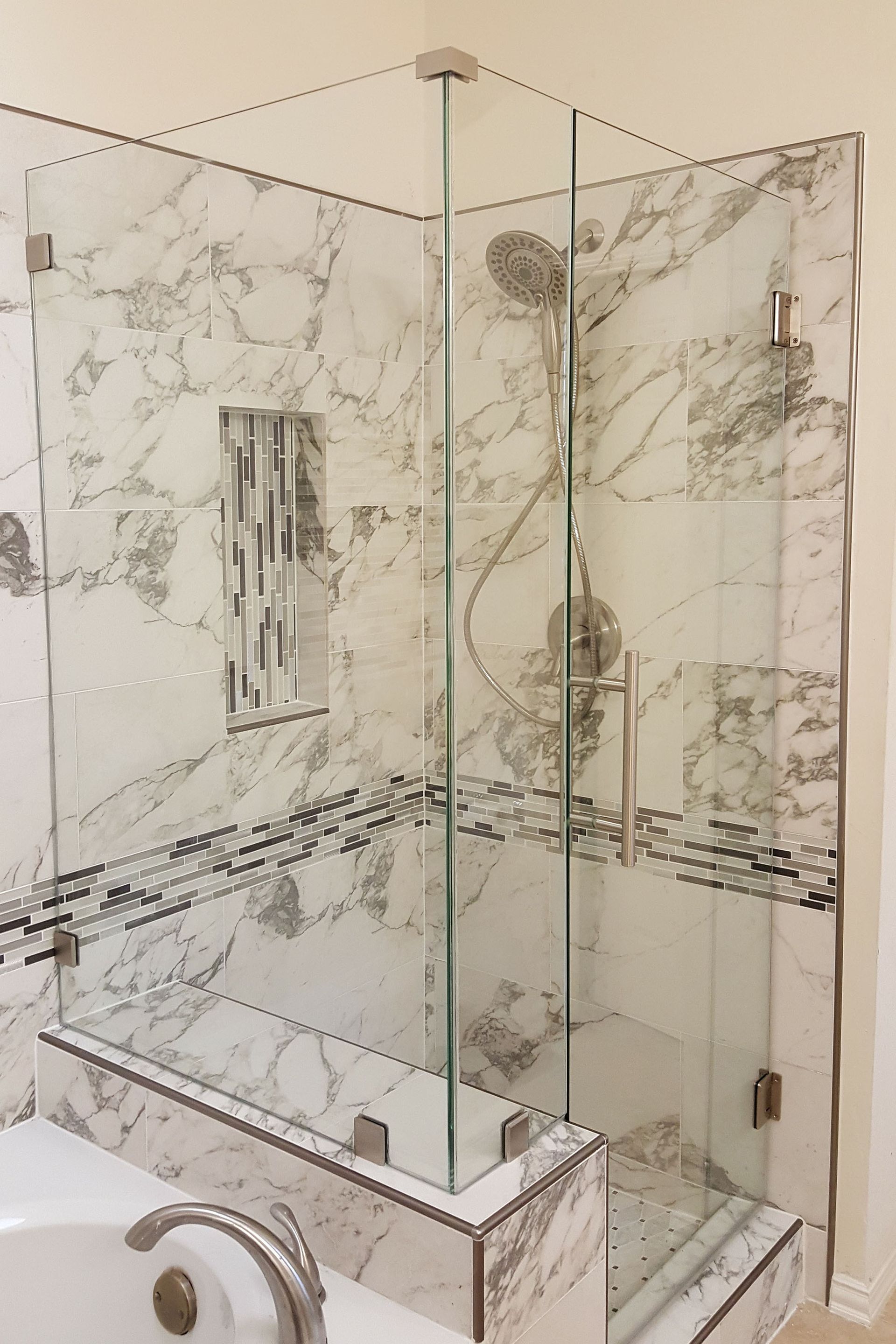 Corner glass shower with marble tile walls and bench.