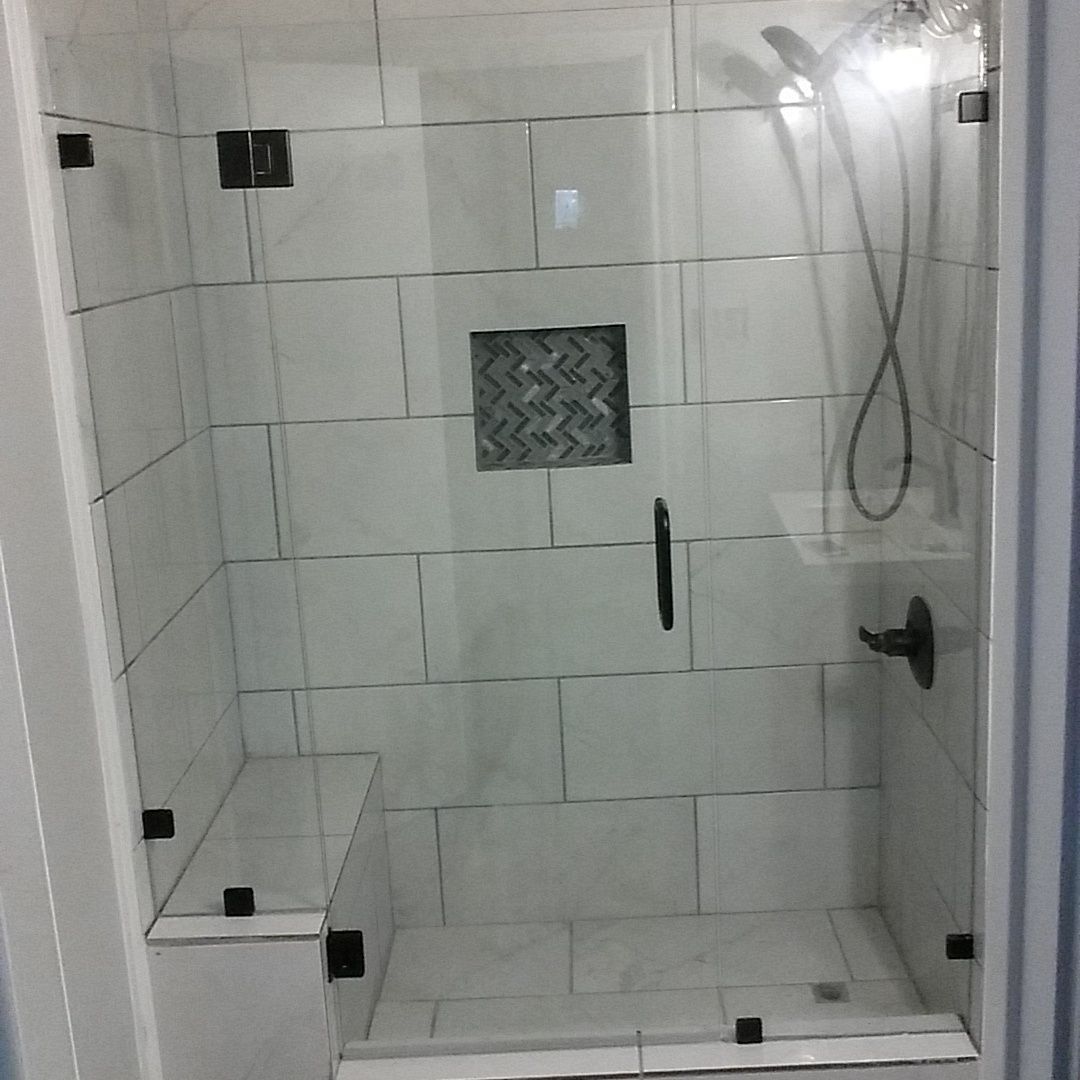 Glass-walled shower with white tiled walls, black hardware, and built-in bench.