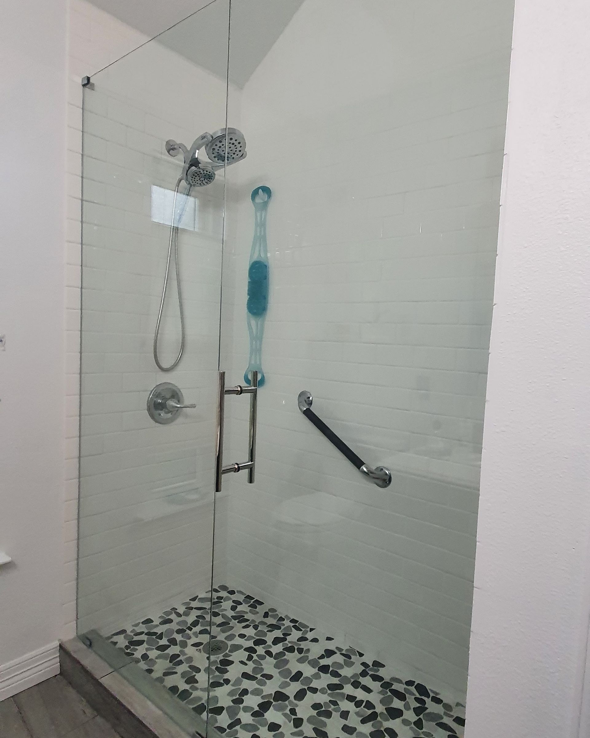 Glass-enclosed shower with pebble floor, silver fixtures, and grab bar.