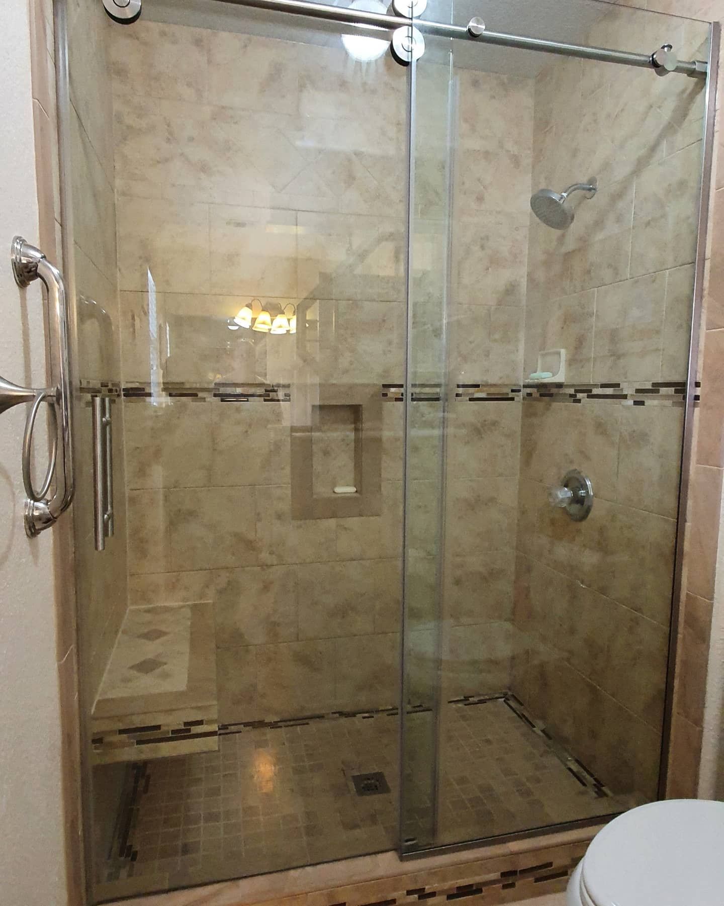 Glass shower with tiled walls and sliding door; shower bench visible.