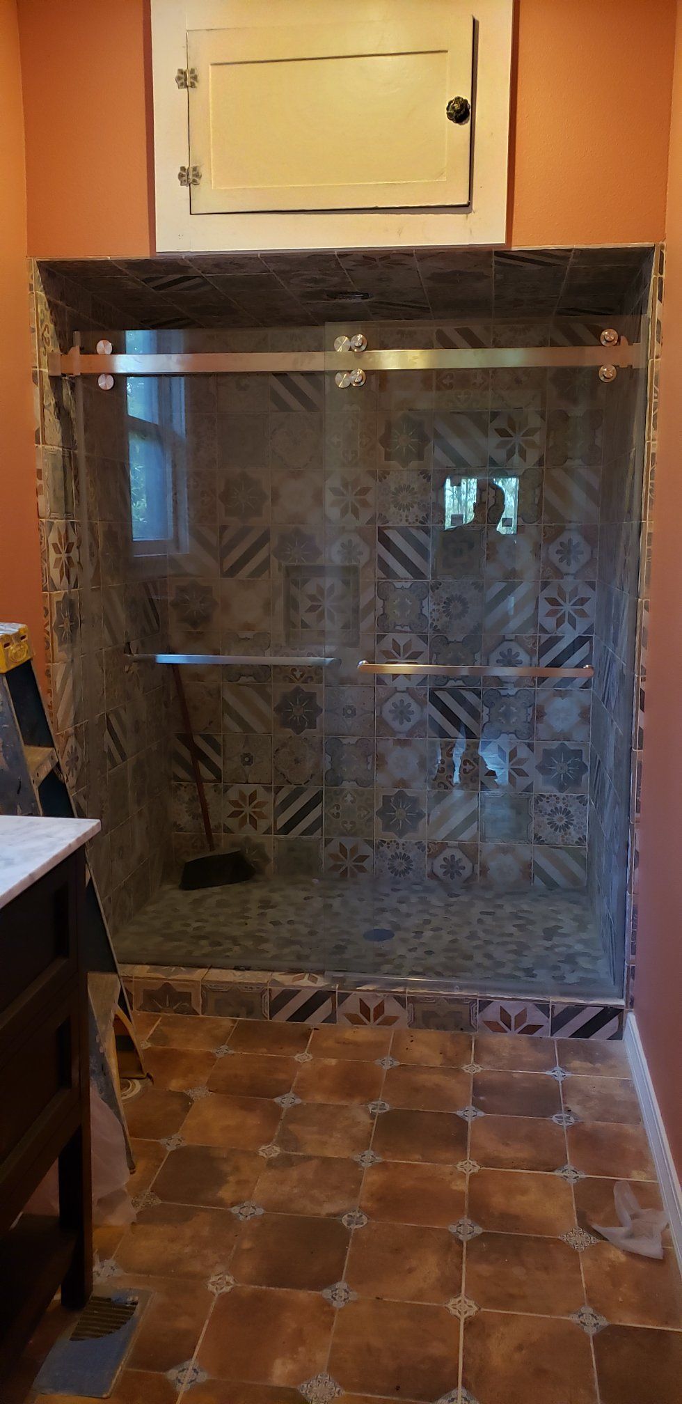 Shower with glass doors and decorative tile, wood frame, set in a bathroom with orange walls.