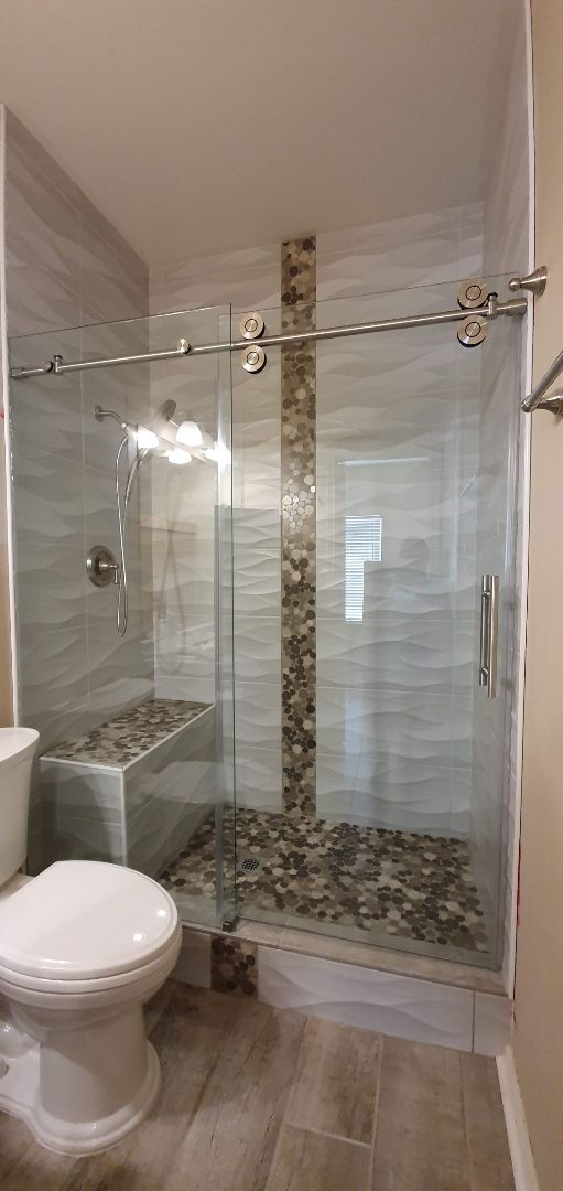Modern bathroom with glass shower, pebble floor, and stone accent wall.