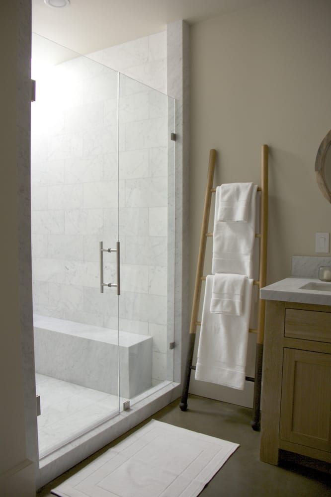 Bathroom with glass shower, towel ladder, vanity, and white towels.