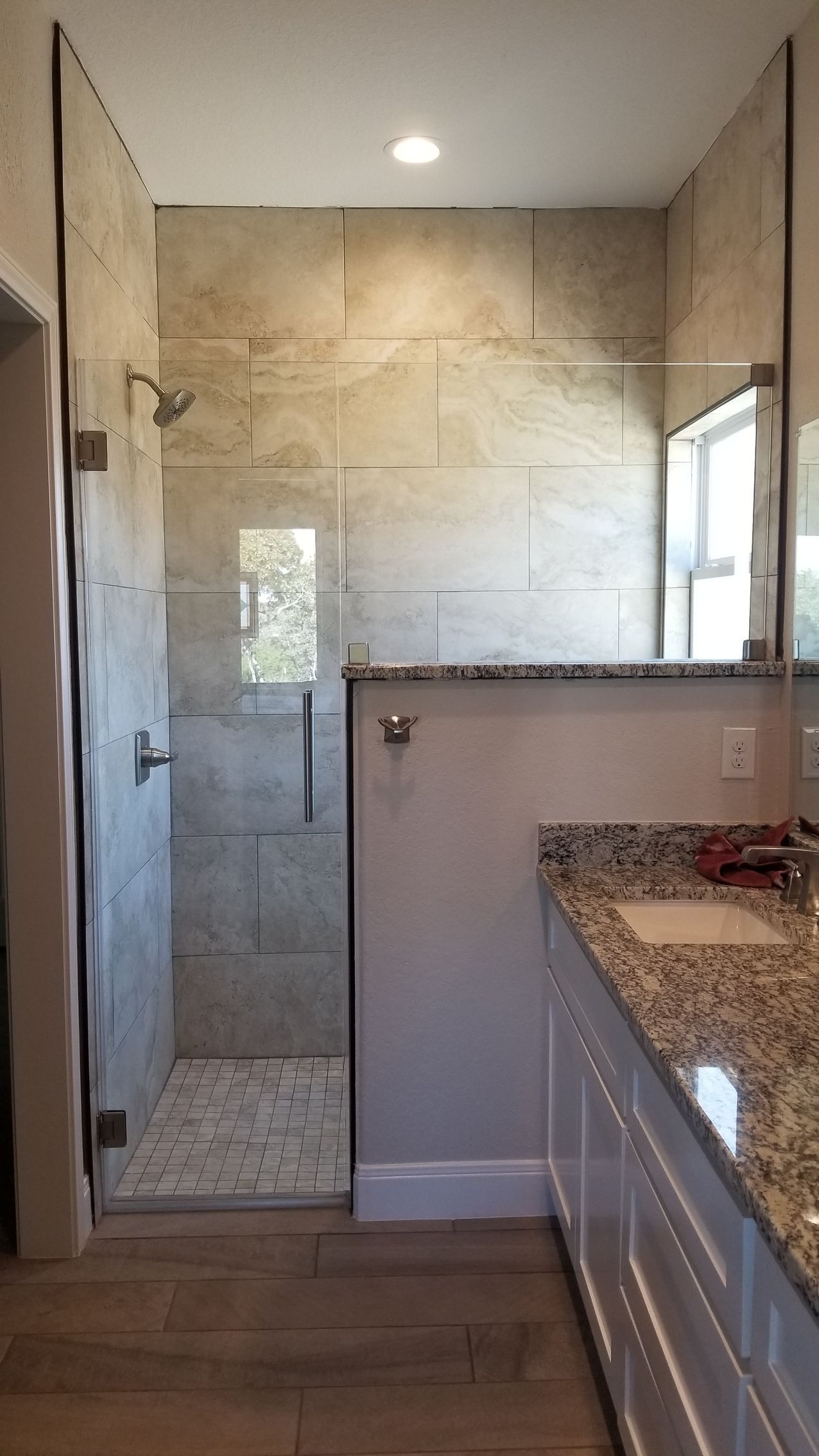Bathroom with a walk-in shower. Beige tile walls, glass door, granite countertop vanity, and wood-look flooring.