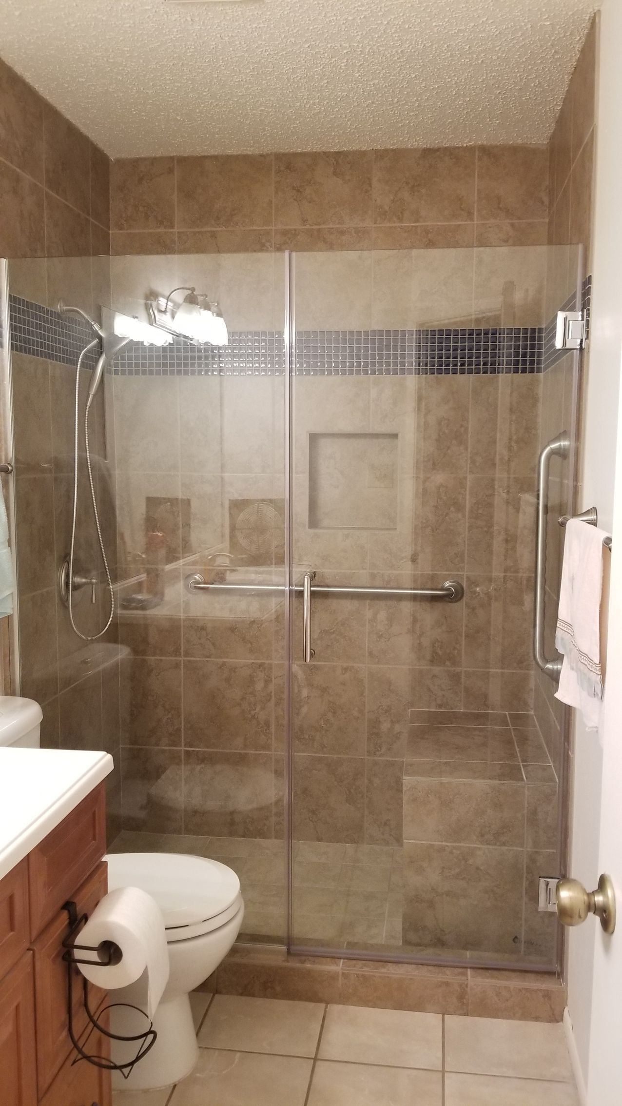 Bathroom with tile walls, glass shower doors, and a toilet.