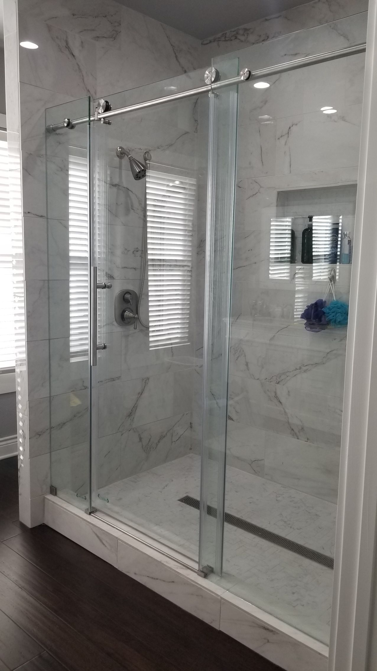 Glass shower enclosure with sliding door and marble-look tile walls.