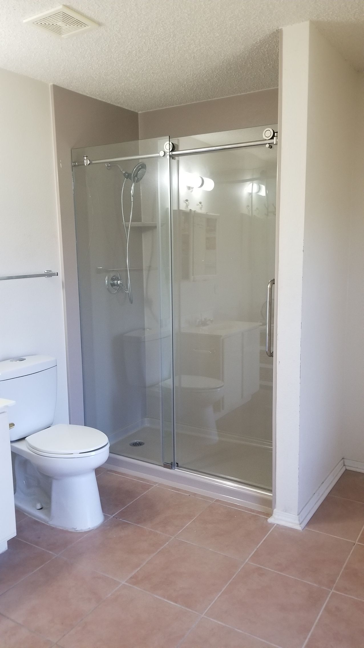 Bathroom with a glass shower enclosure, toilet, and brown tile floor.