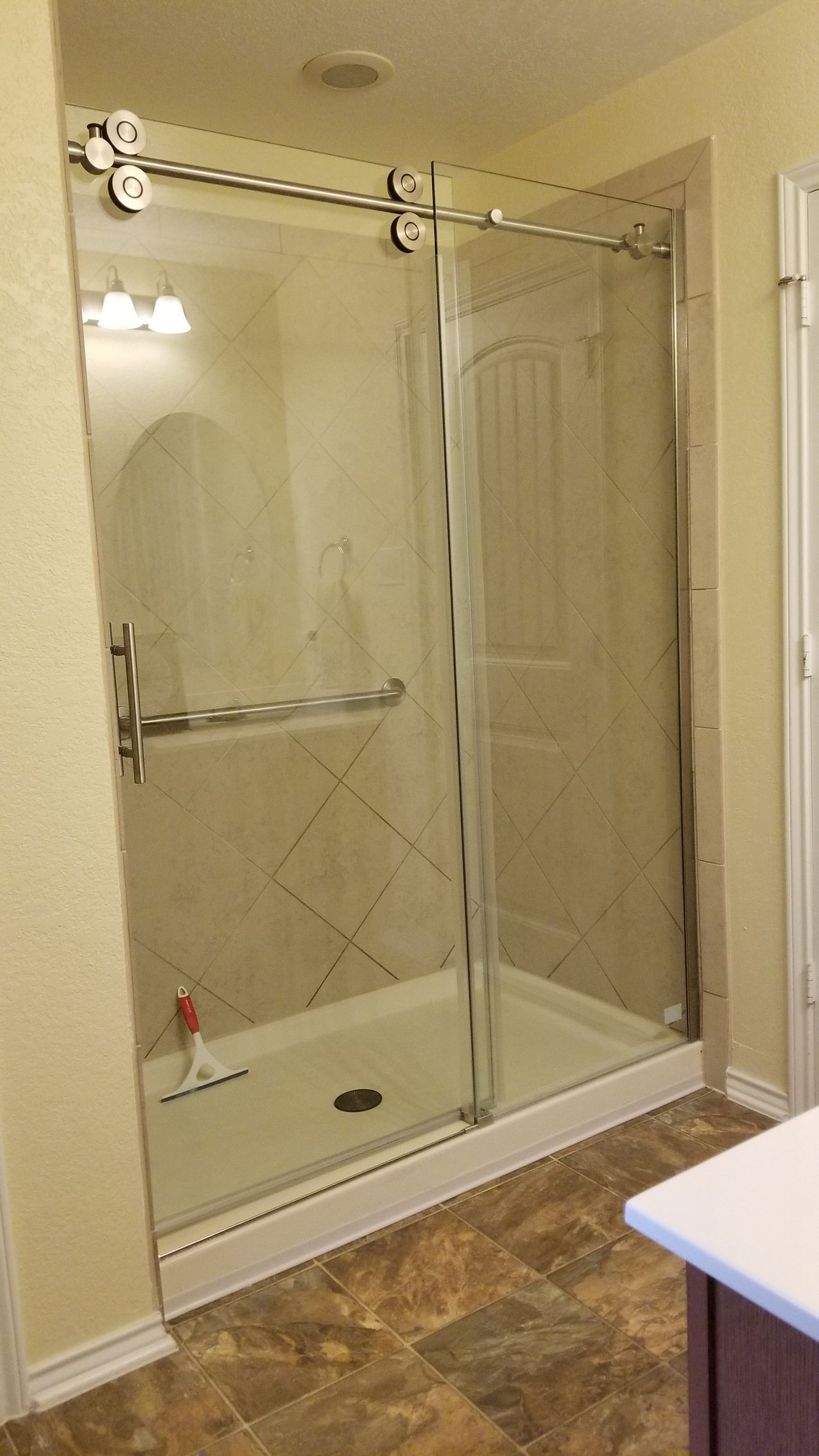 Shower stall with sliding glass doors, white frame, beige tile, and light fixture.