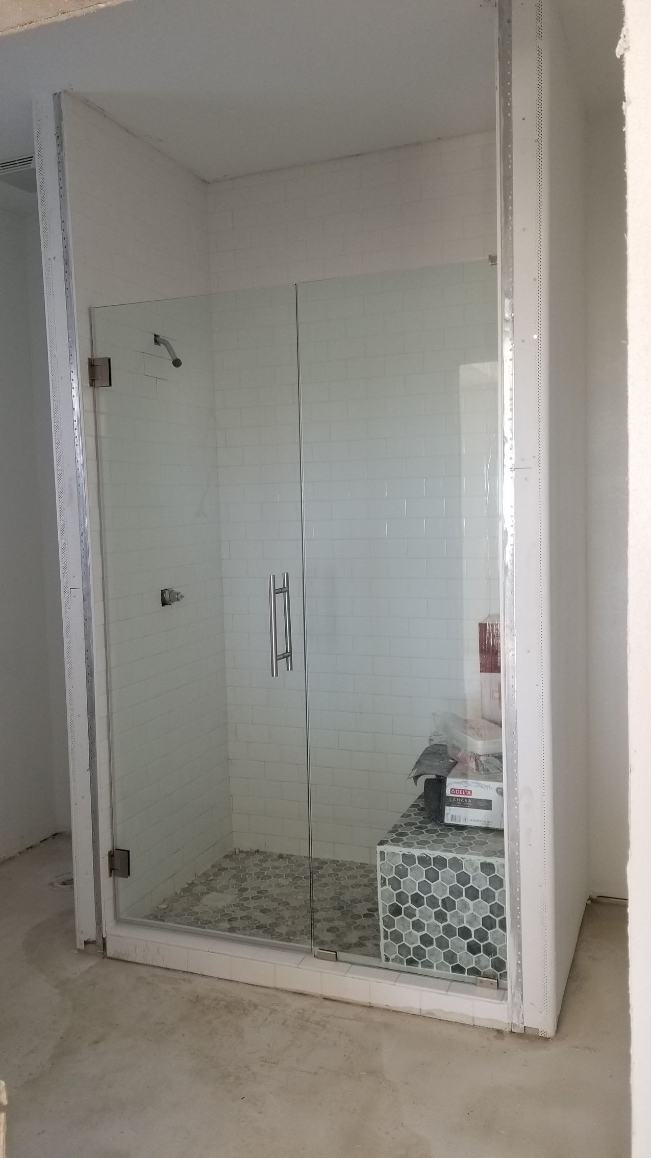 Glass shower stall in a bathroom under construction; white walls and mosaic tiled floor.