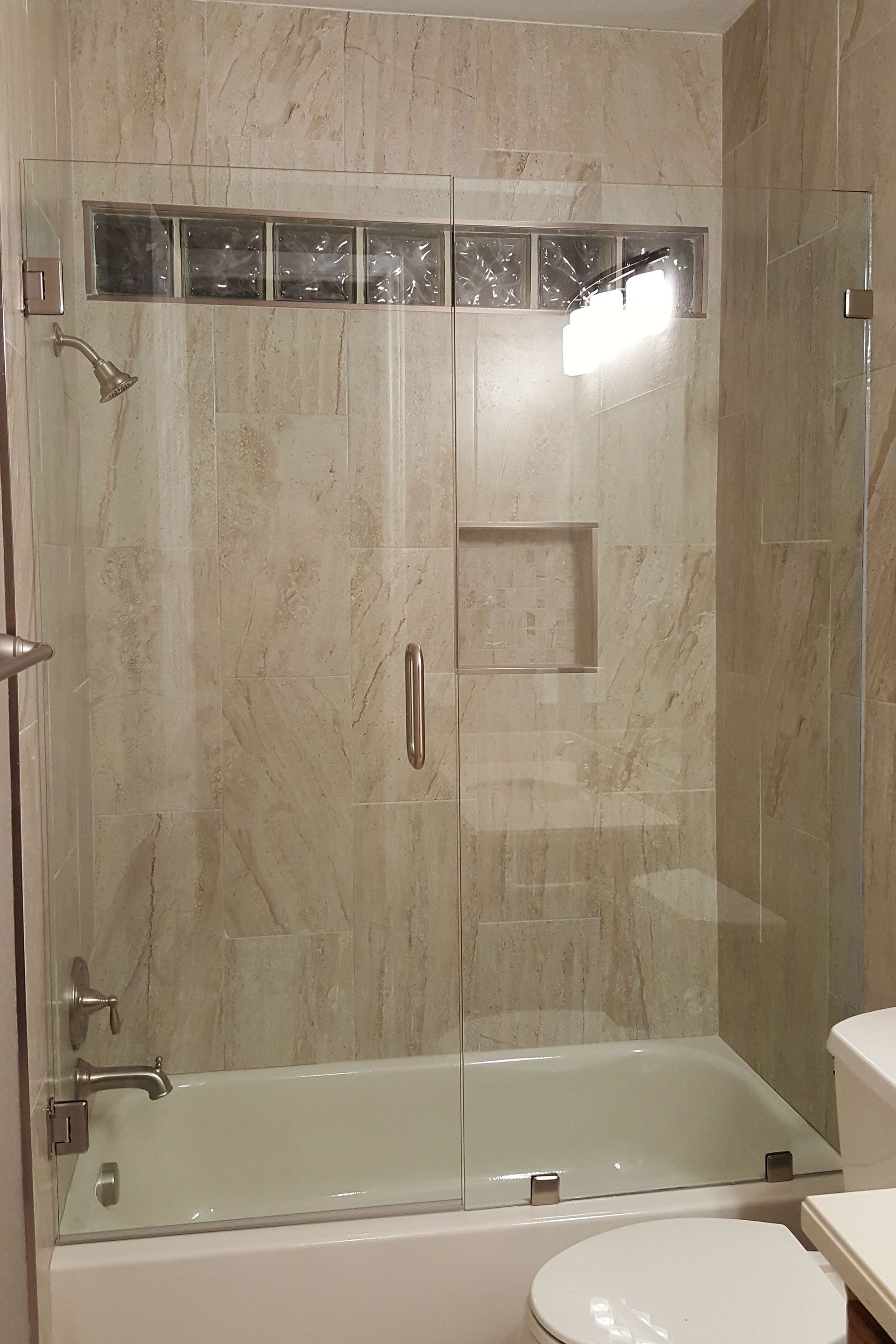 Shower with glass doors and a glass block window above, beige tile walls, and a white bathtub.