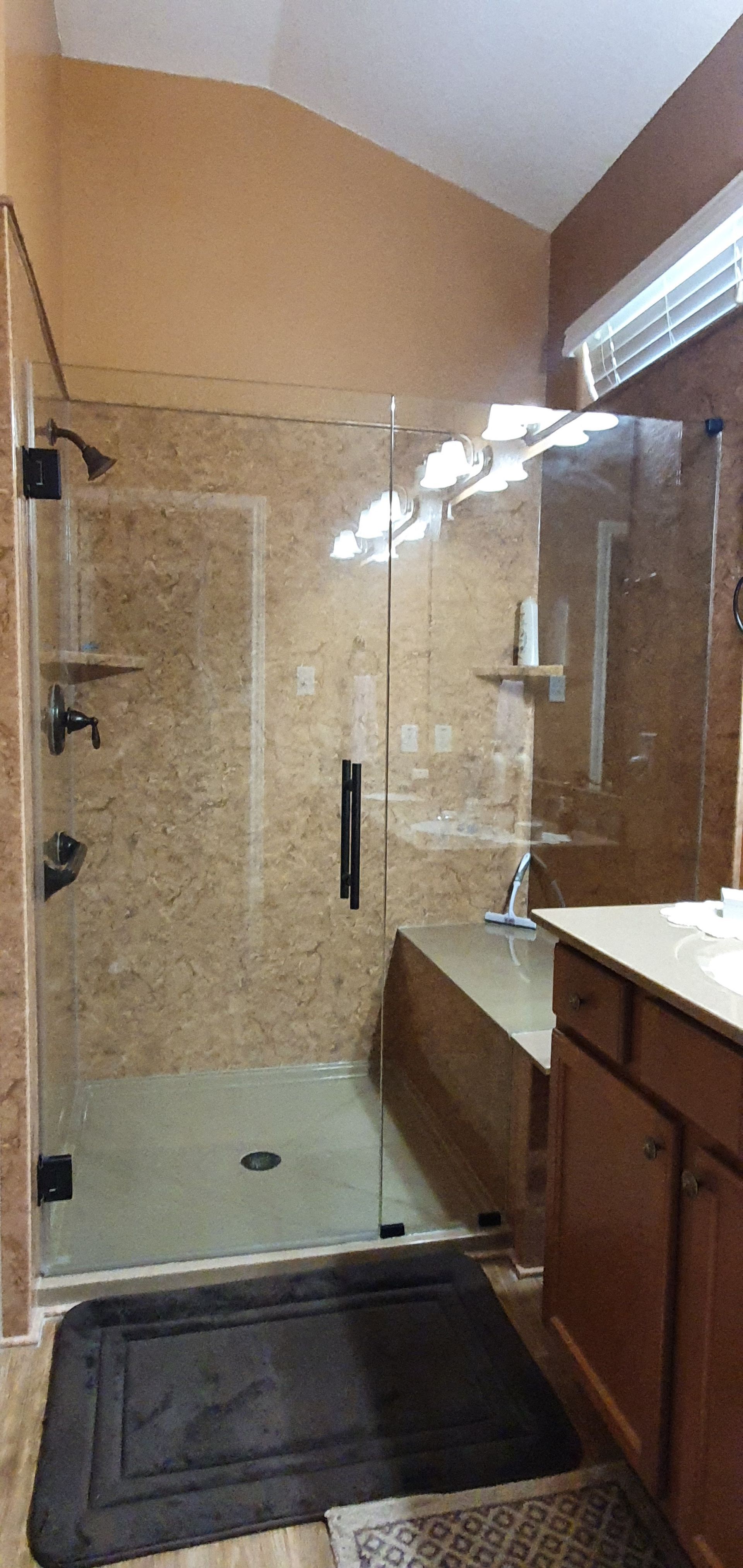 Bathroom with a large, glass-enclosed shower, featuring brown tile, a shower bench, and dark fixtures.