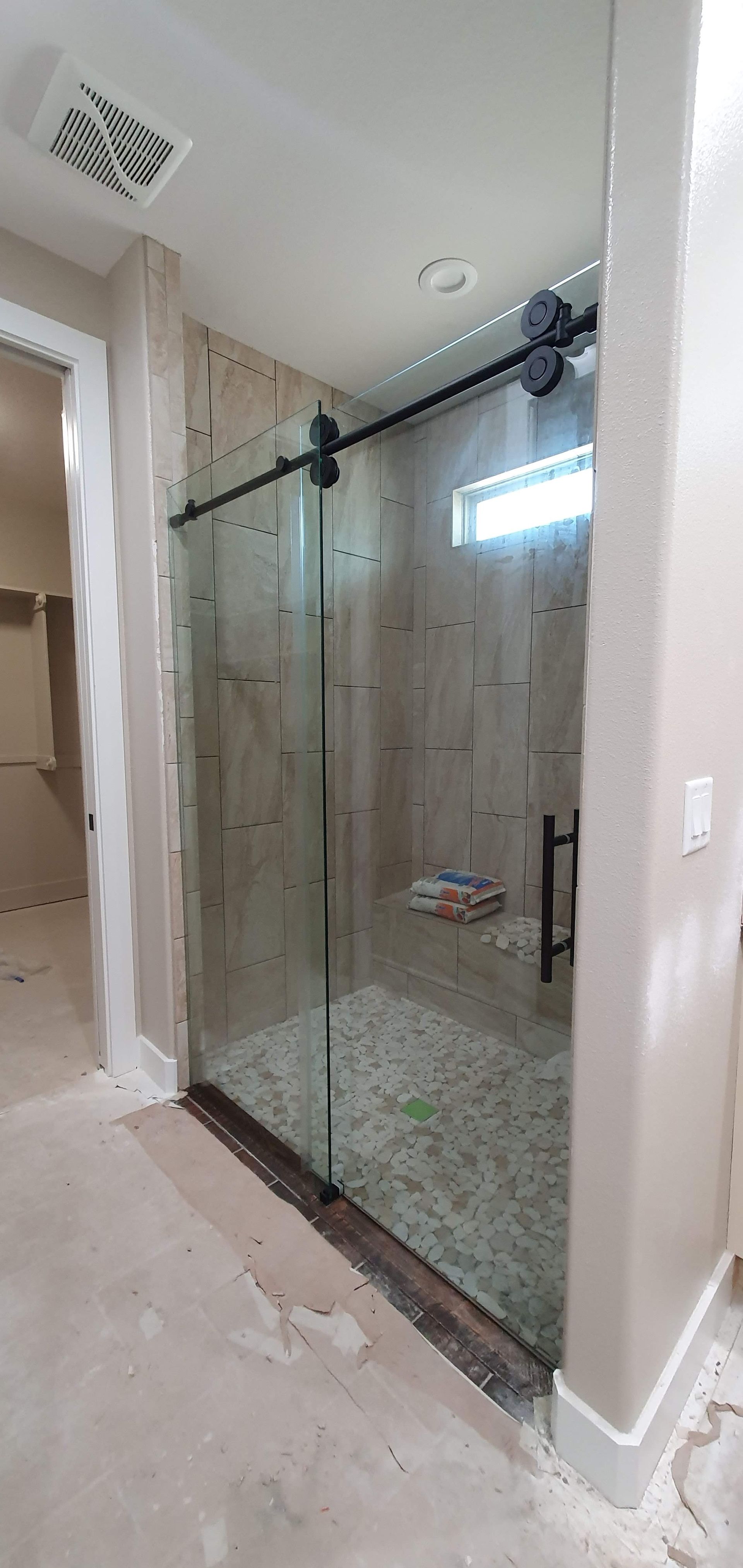 A sliding glass shower door in a bathroom. The shower has stone tile walls and a pebble floor.