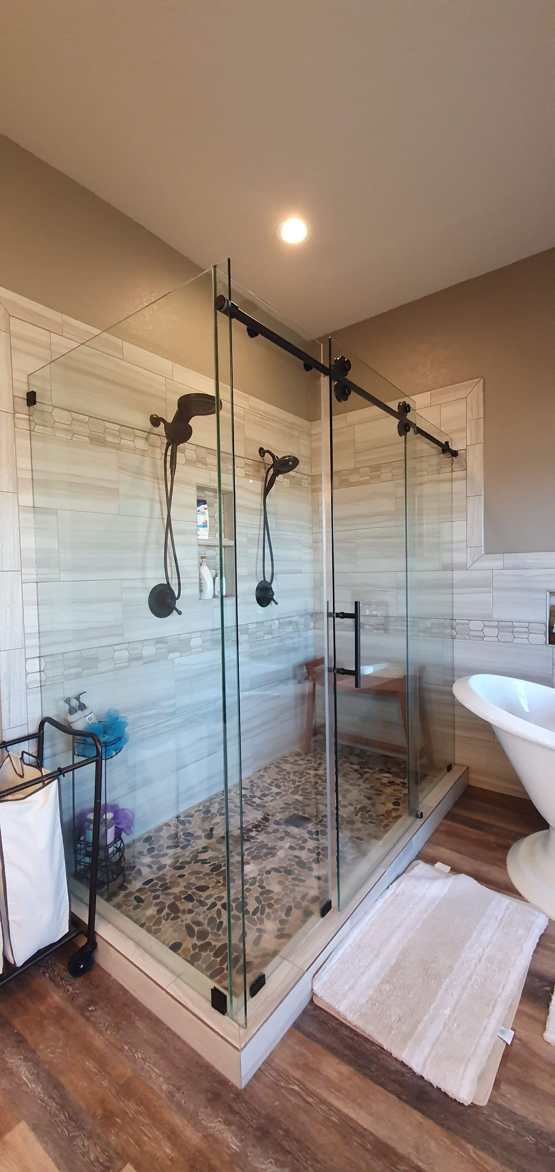 Modern bathroom with a glass-enclosed shower, stone flooring, and a white rug.