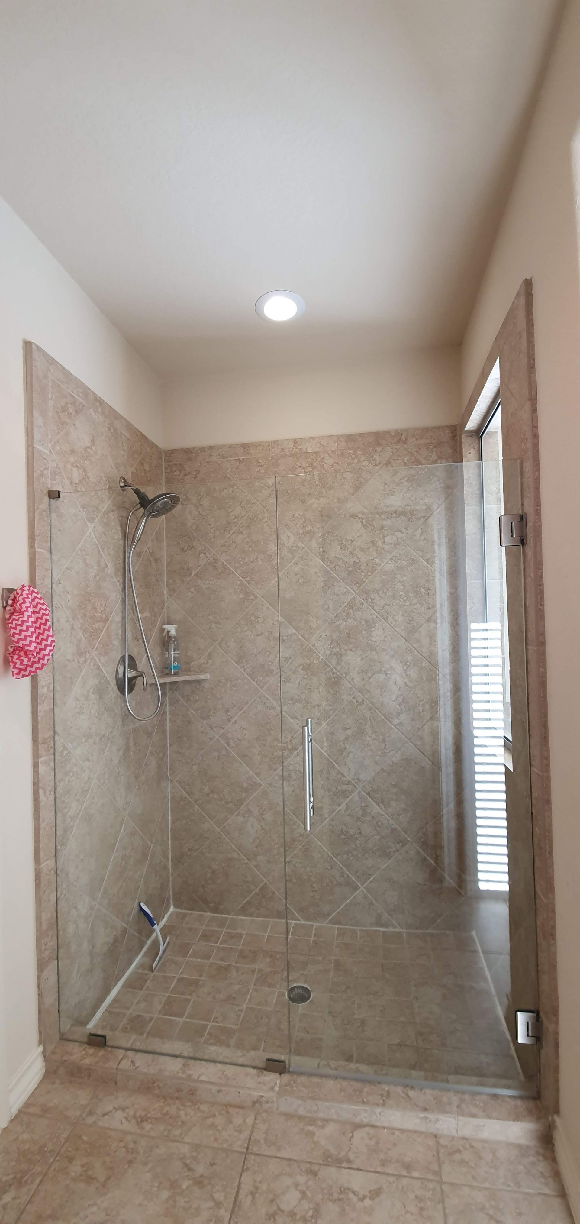 A walk-in shower with glass doors and beige tile walls. The ceiling has a recessed light.