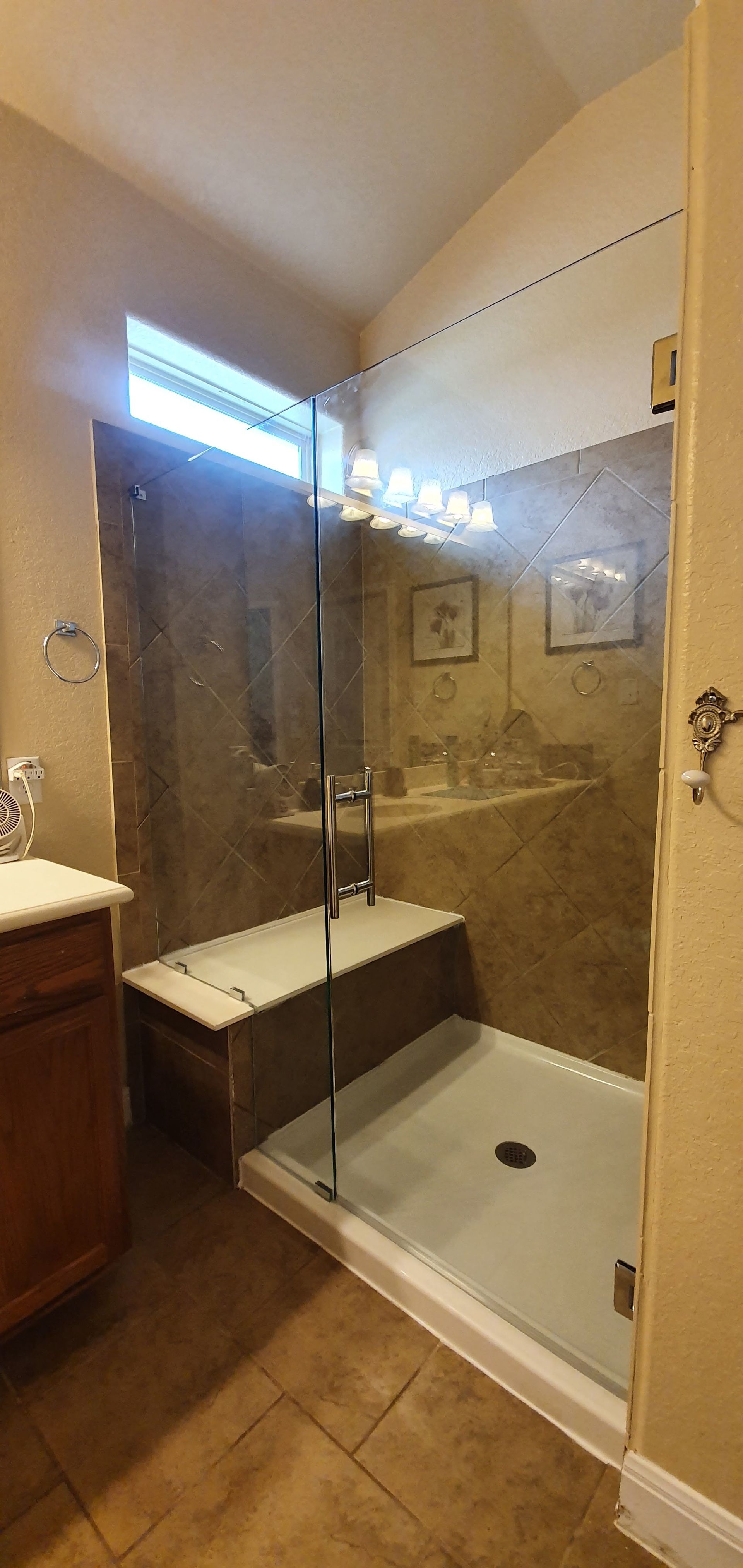 A modern bathroom with a glass shower enclosure and bench, beige tile walls, and a white shower pan.