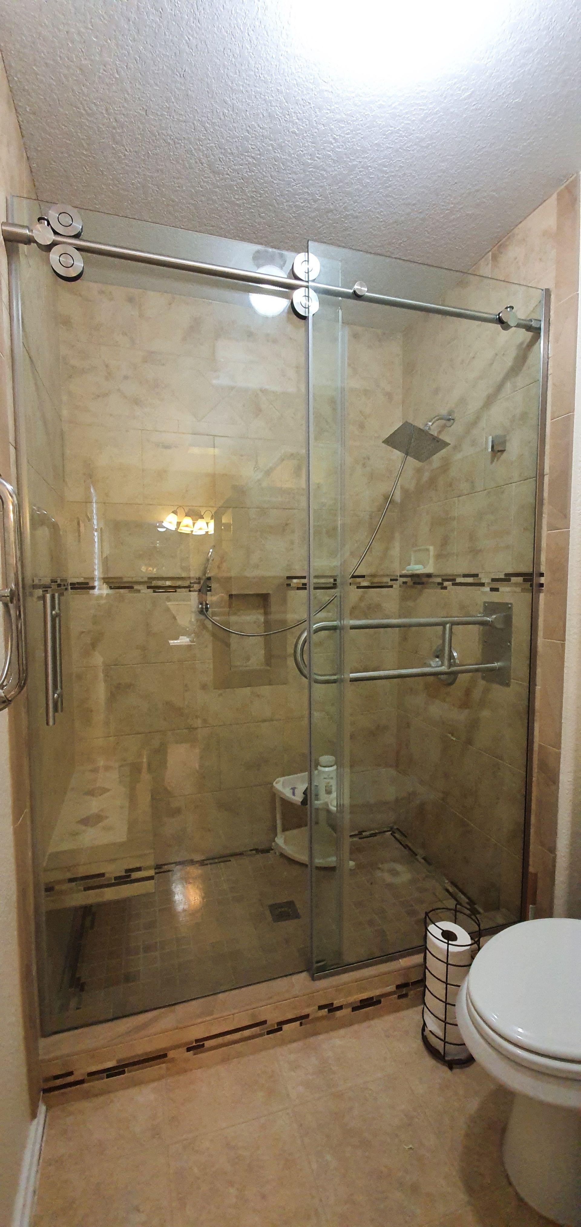 A bathroom with a glass shower enclosure and a toilet. Beige tile is on the floor and walls.