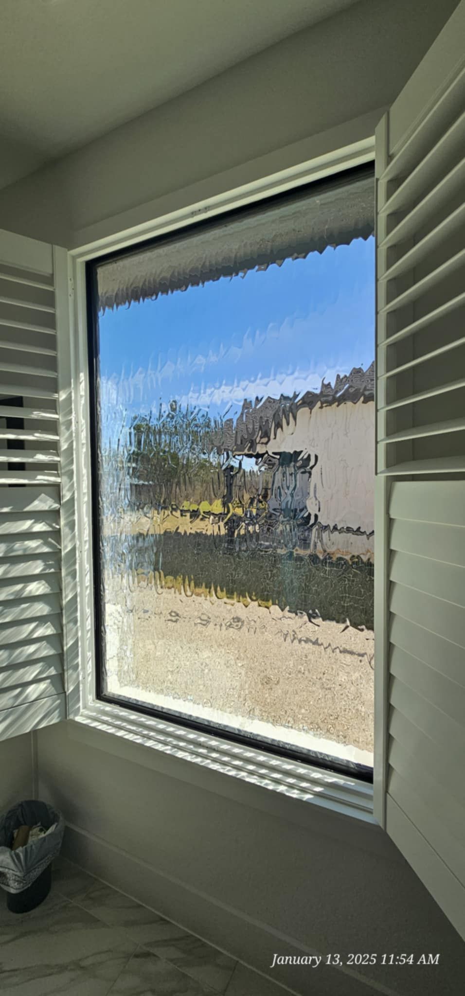 Window with white shutters open, revealing a view of blue sky and a landscape.