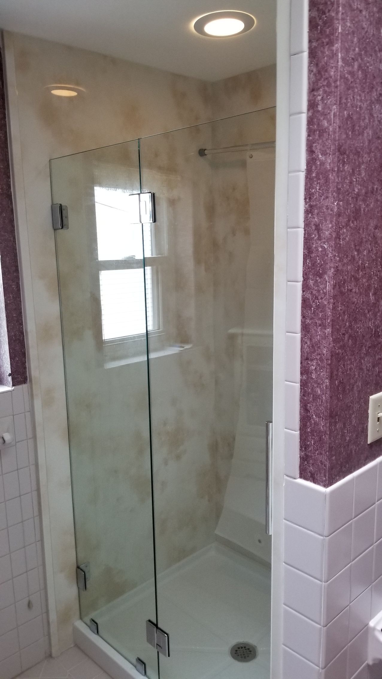 Glass shower enclosure with white tile and decorative wall behind.
