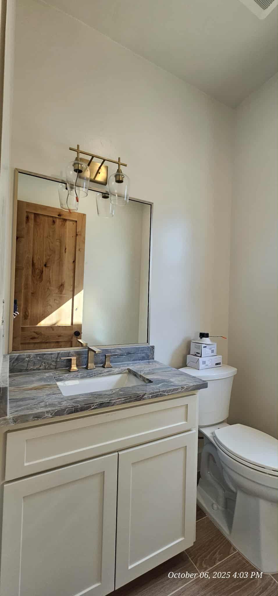 Bathroom with a white vanity, granite countertop, mirror, and toilet. Wooden door visible.
