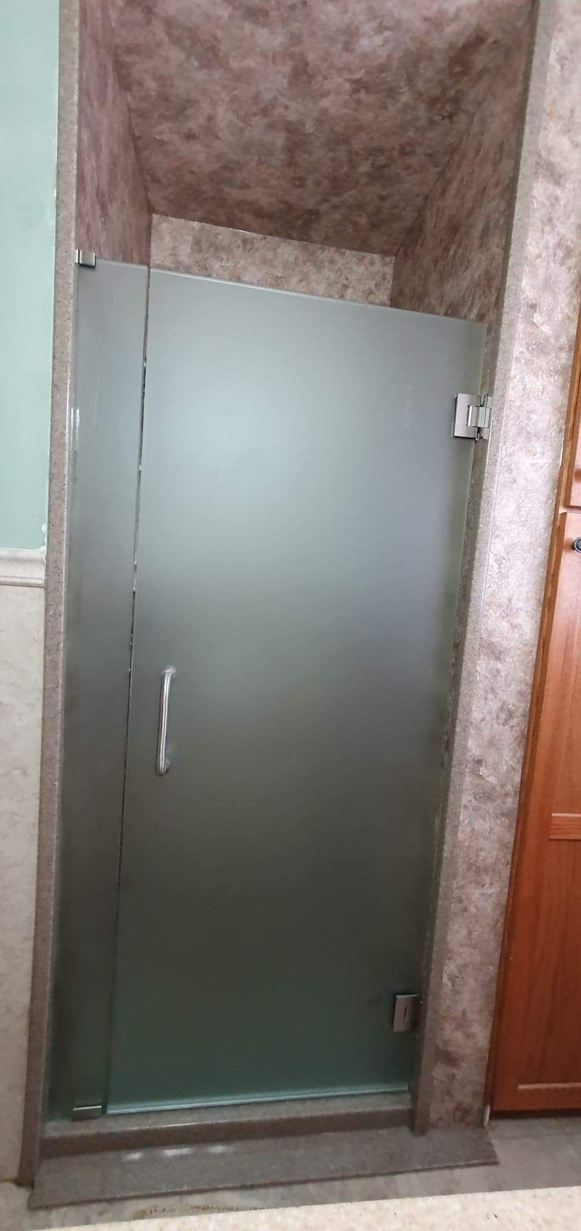 Frosted glass shower door in a bathroom with textured brown walls.