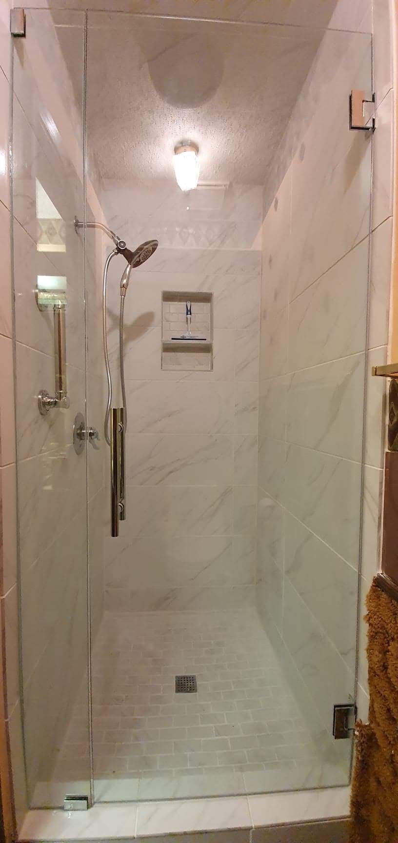 Glass shower with white tile walls and floor. Chrome shower fixtures. Clear glass doors.