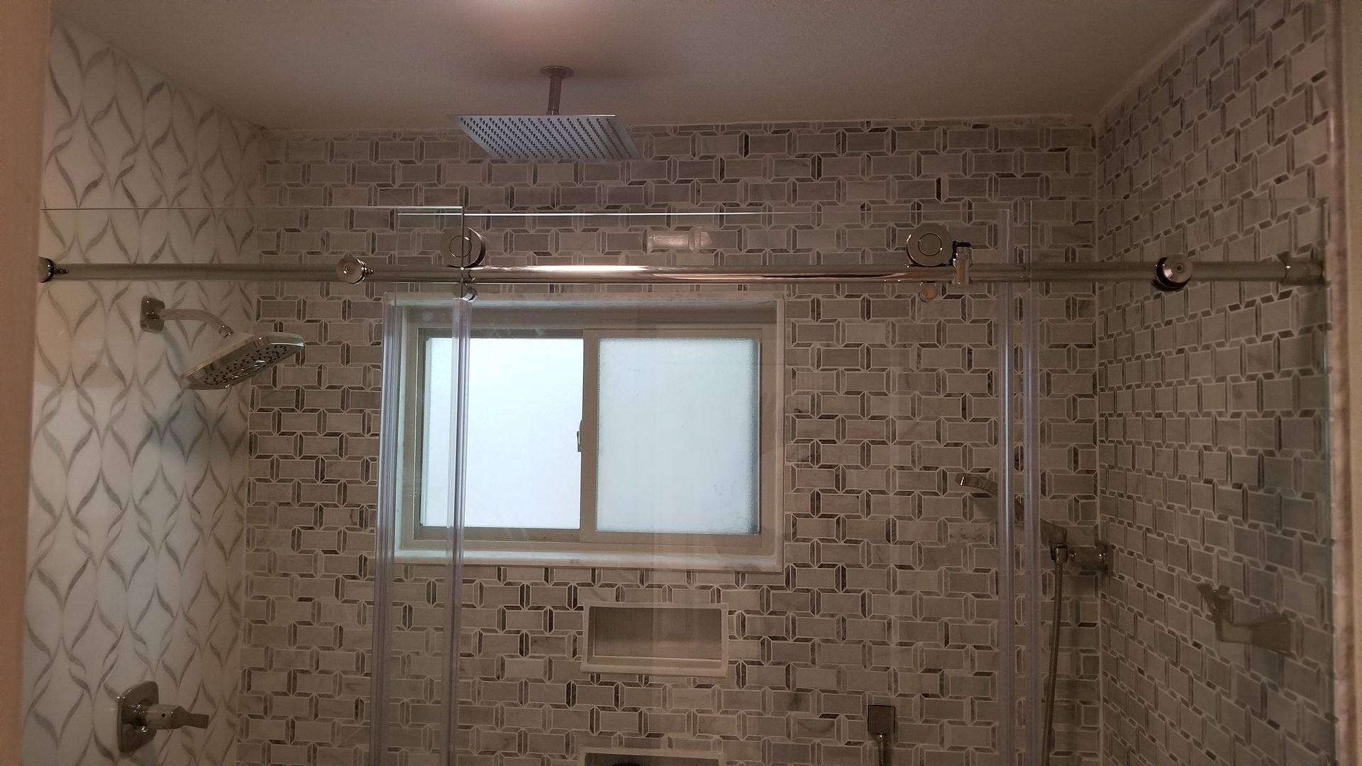Bathroom shower with patterned tile walls, glass doors, a window, and multiple shower heads.