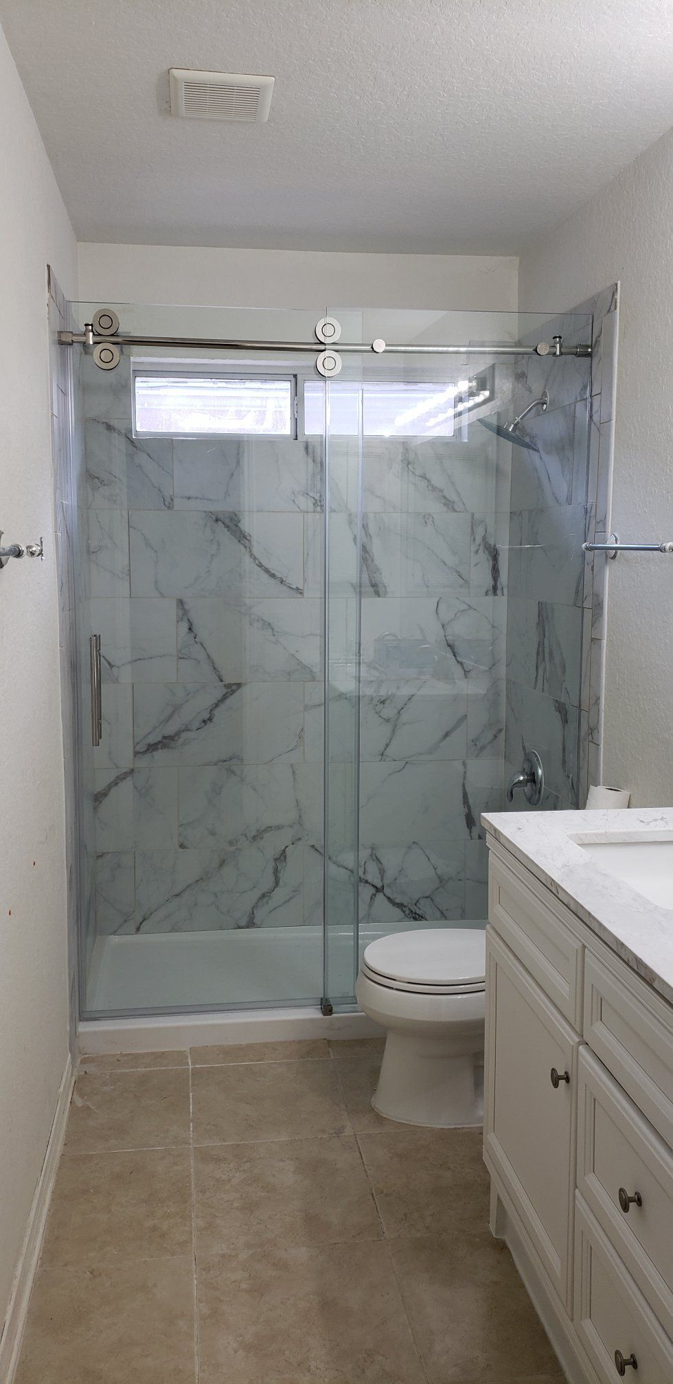 Bathroom with a marble-patterned glass shower, white toilet, and vanity with a light-colored floor and walls.
