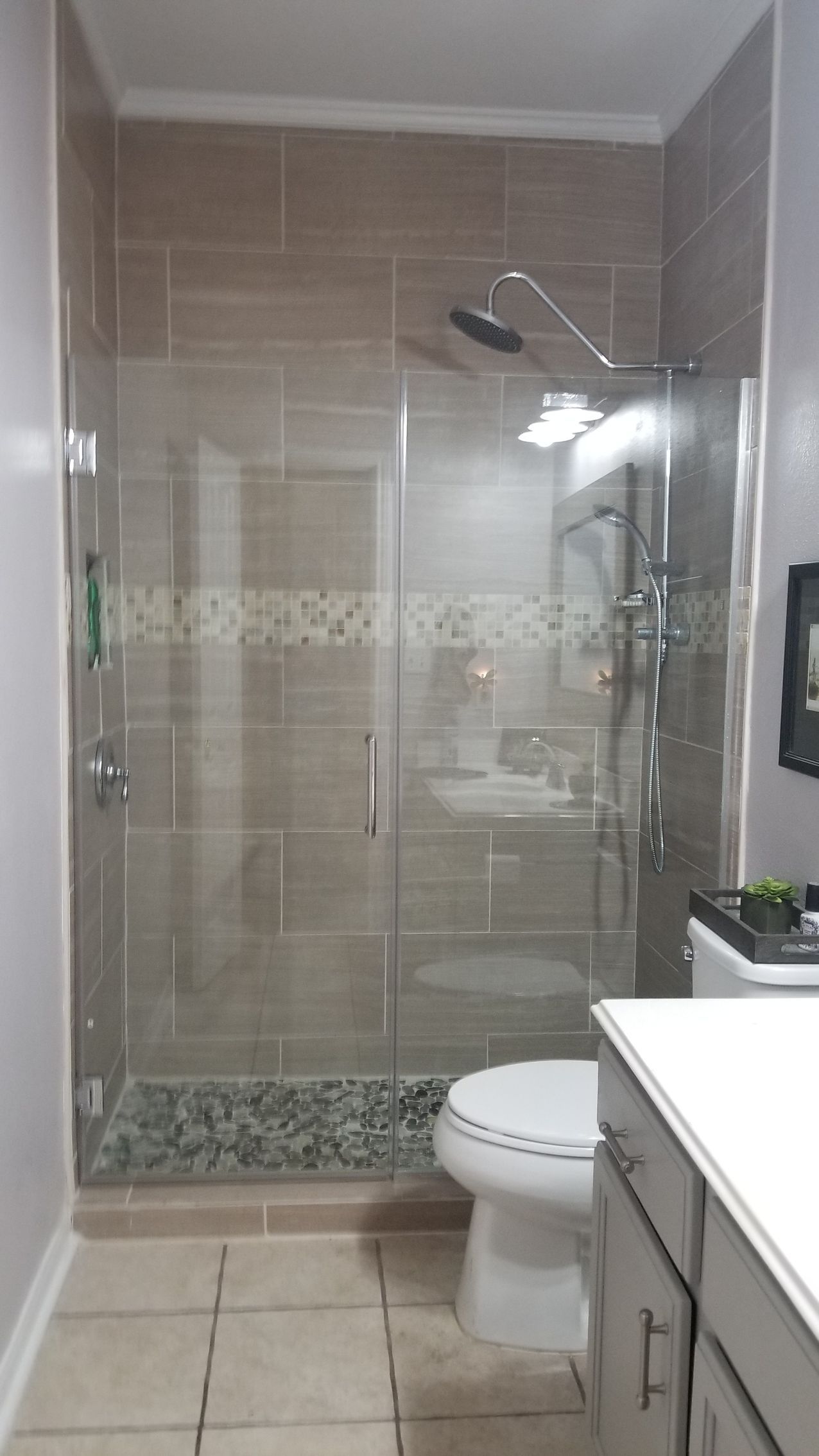 Shower with glass door, beige tile, stone floor, toilet, vanity.