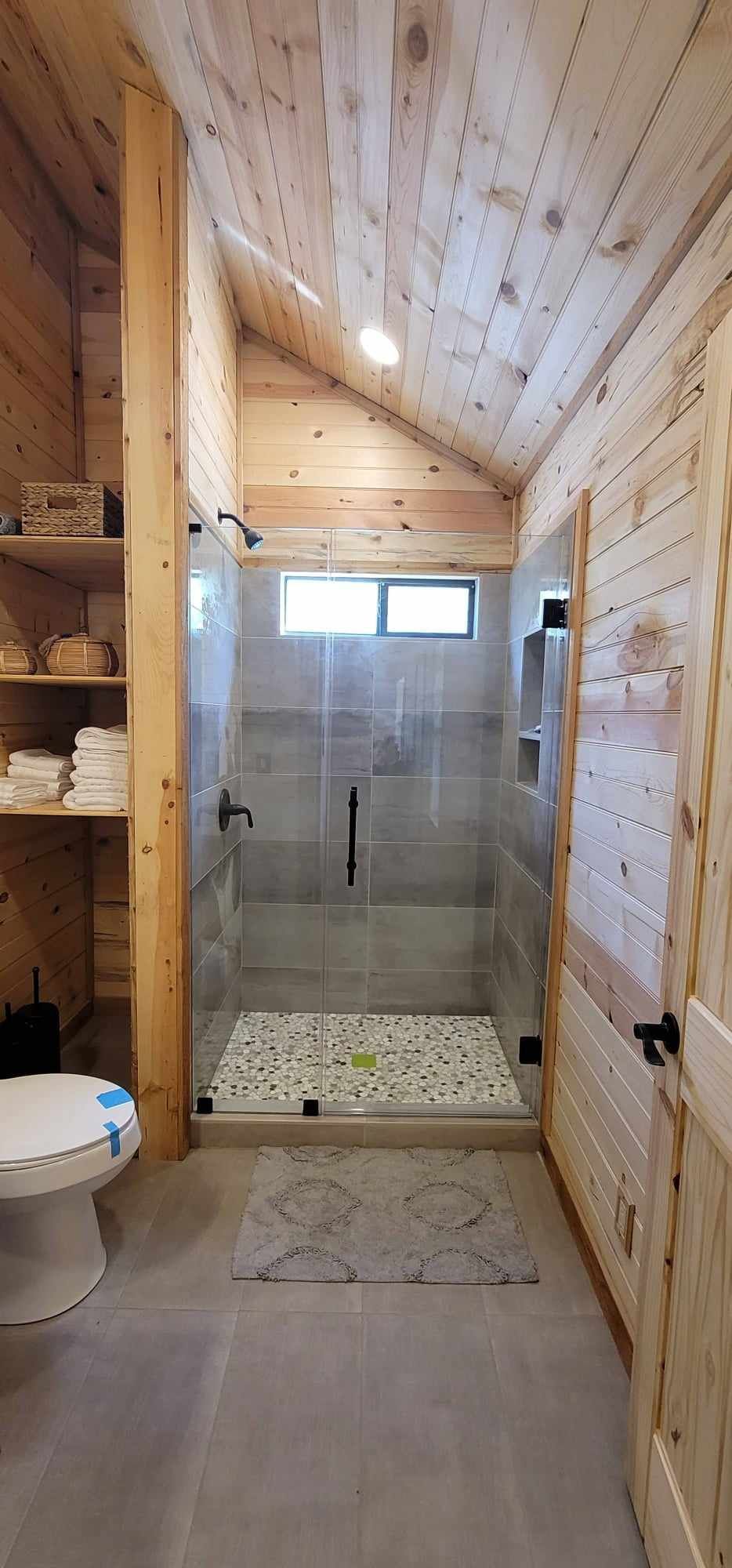 Rustic bathroom with wood paneling, gray tile shower, and pebble floor.