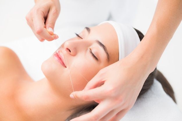 A woman is getting a threading treatment on her face.