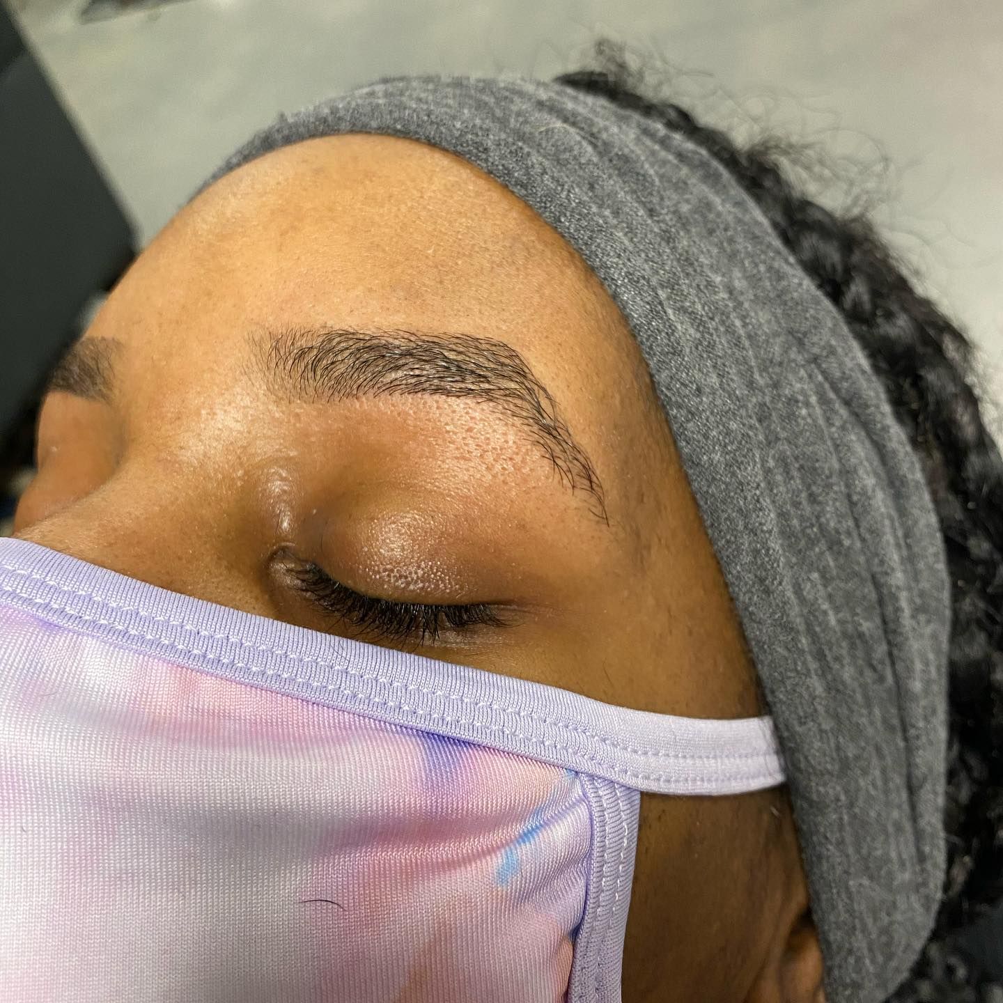 A woman is getting her eyebrows drawn by a tattoo artist.
