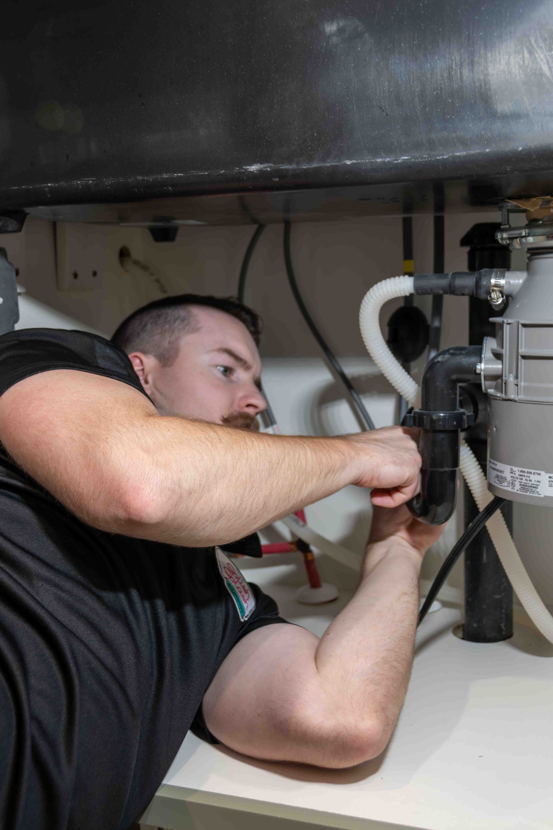 Plumber working under a kitchen sink, tightening a pipe fitting.