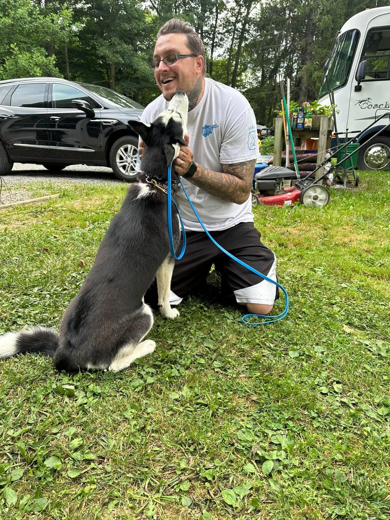 A man is kneeling down next to a dog on a leash.