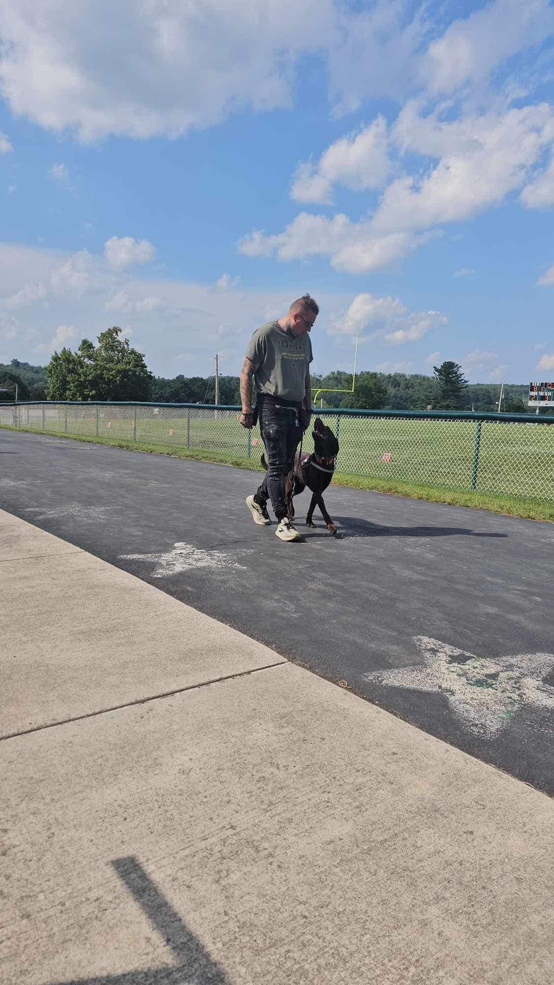 A man is walking a dog on a leash down a sidewalk.