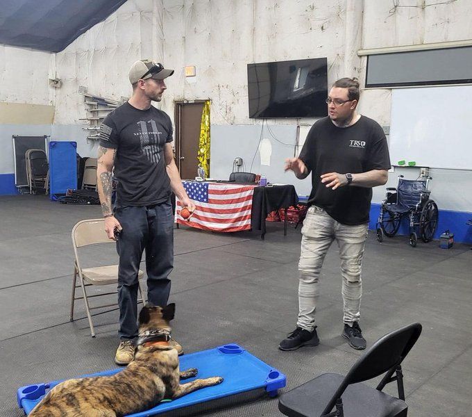 Two men are talking to a dog that is laying on a blue mat