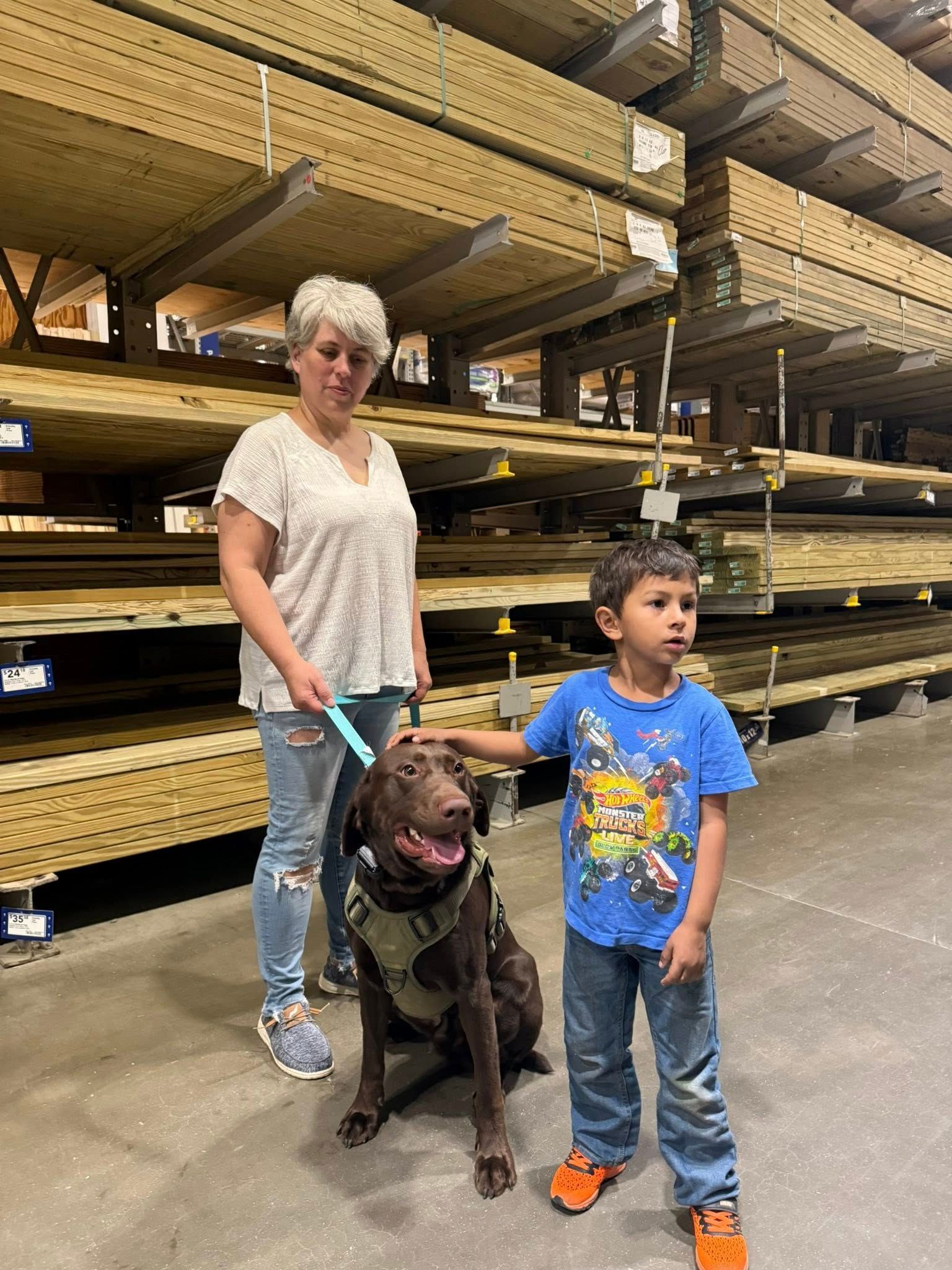 A woman and a boy are standing next to a dog in a warehouse.