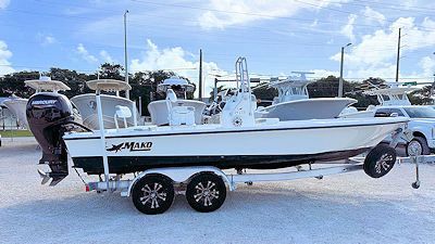 White Mako boat on a trailer, black motor, parked outside, blue sky background.