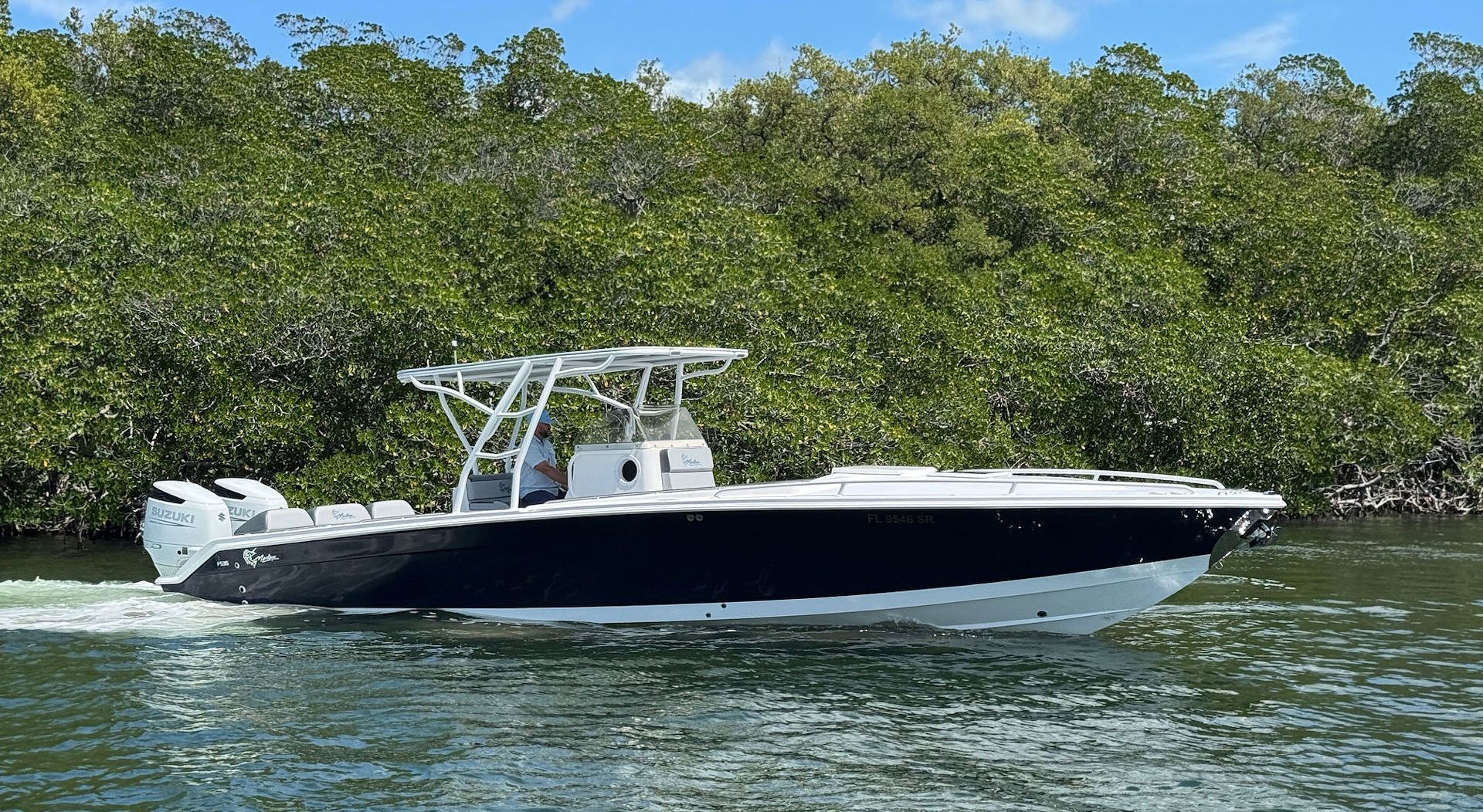 A dark blue and white center console motorboat with twin outboard engines cruising along a mangrove coastline.